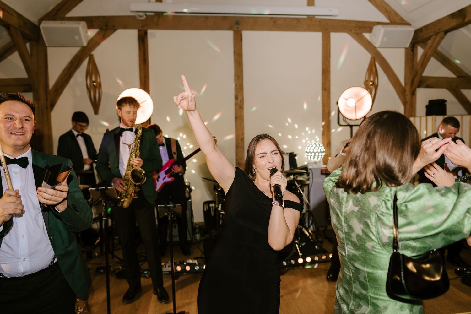 Live wedding band performing with saxophonist, guitarist, and singer raising hand on dance floor with sparklers.