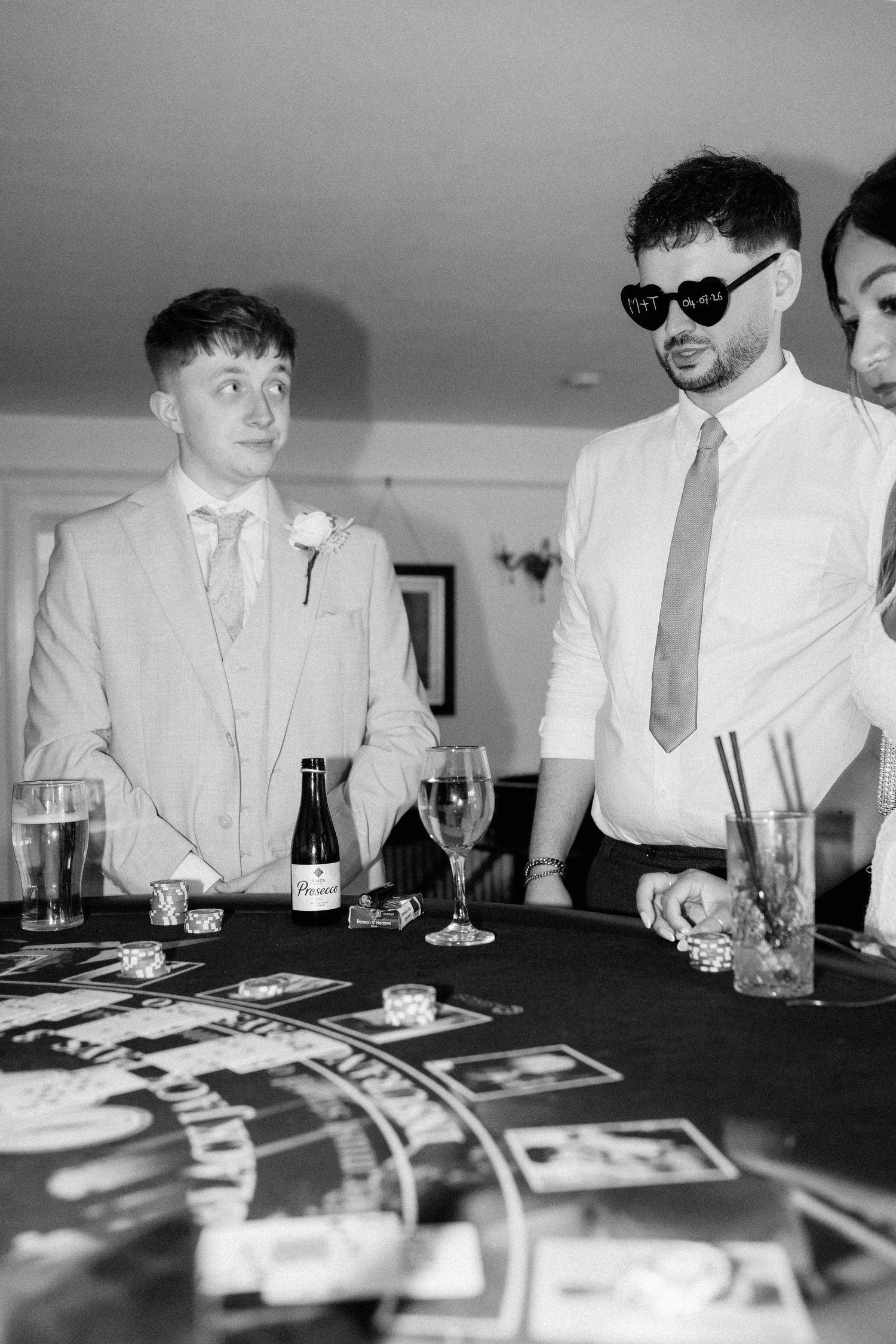 Black and white photo of wedding guests playing blackjack at casino table during wedding reception.