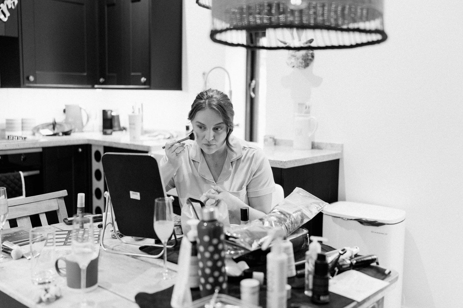 Woman sitting at a cluttered table reading a book in a modern kitchen, captured in black and white photography.