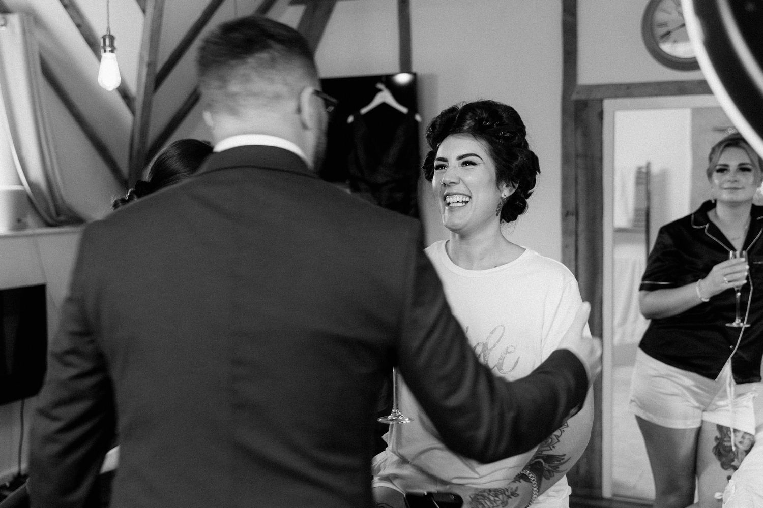 Black and white photo of a bride laughing with a groom during wedding preparations indoors.