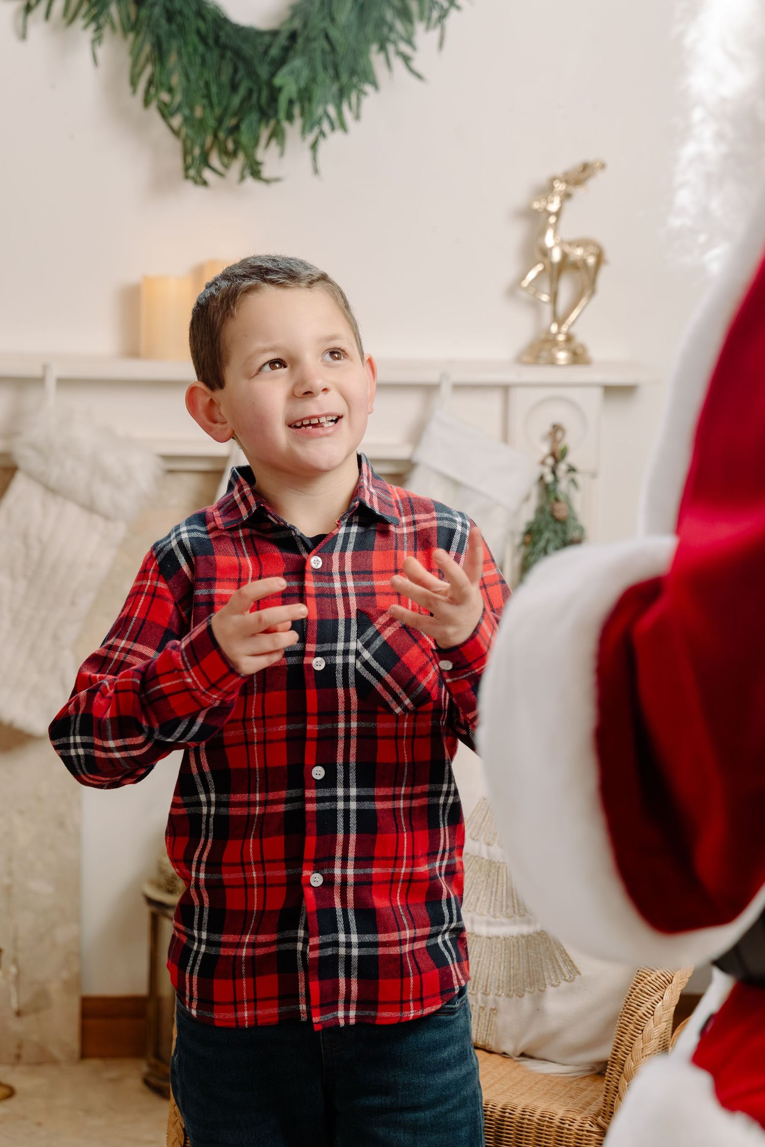 Excited young boy in red plaid shirt reacting with joy while meeting Santa Claus in a festive Christmas decorated room.