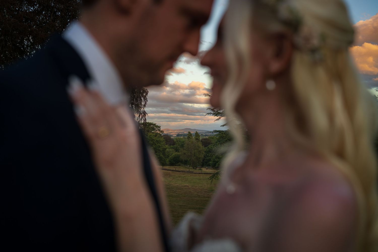 Romantic wedding couple sharing an intimate moment with a stunning sunset sky and lush green landscape in the background.