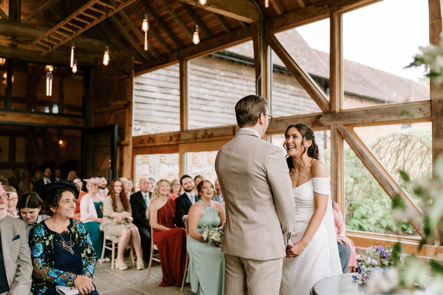 Bride and groom holding hands and smiling during their wedding ceremony in a rustic wooden barn.