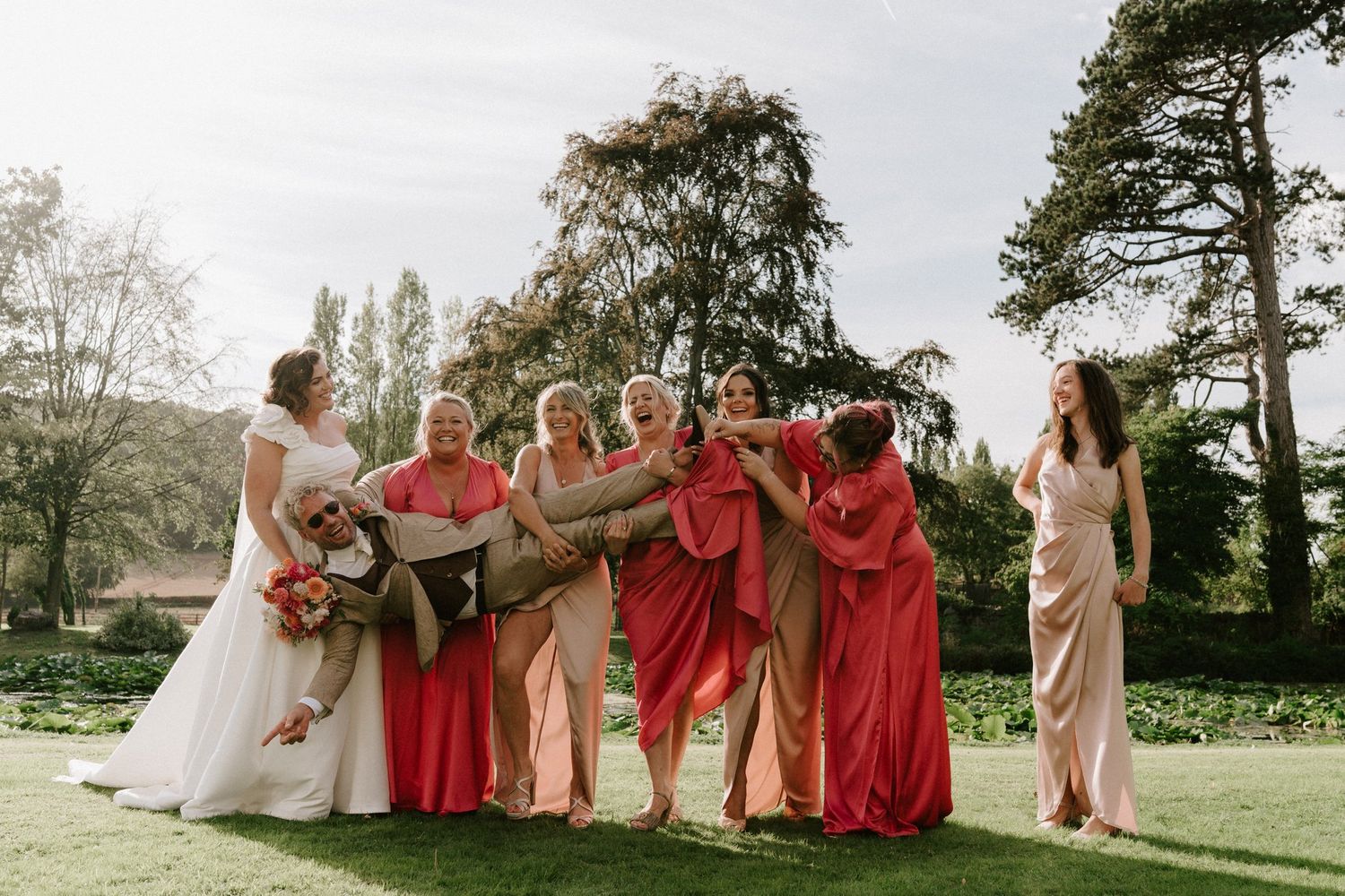 Bridesmaids lifting the groom off his feet on the lawn at Brinsop Court