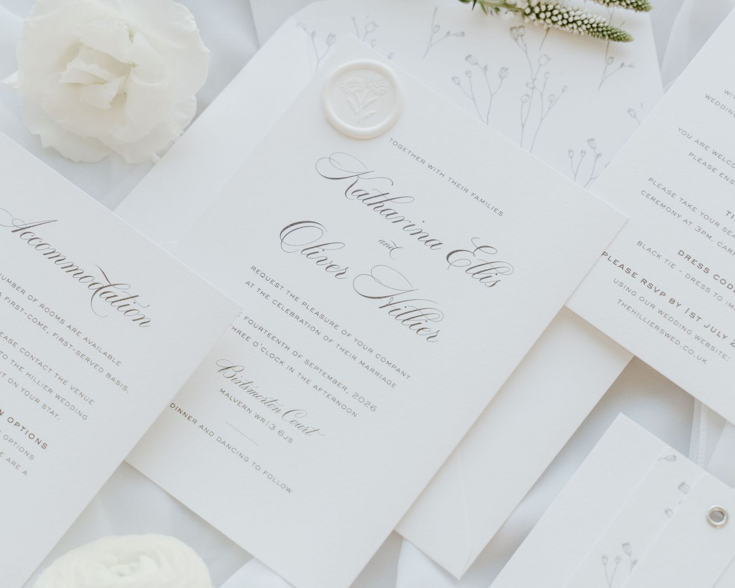 Elegant white wedding invitation suite with calligraphy script, wax seal, and floral accents on a soft white background.