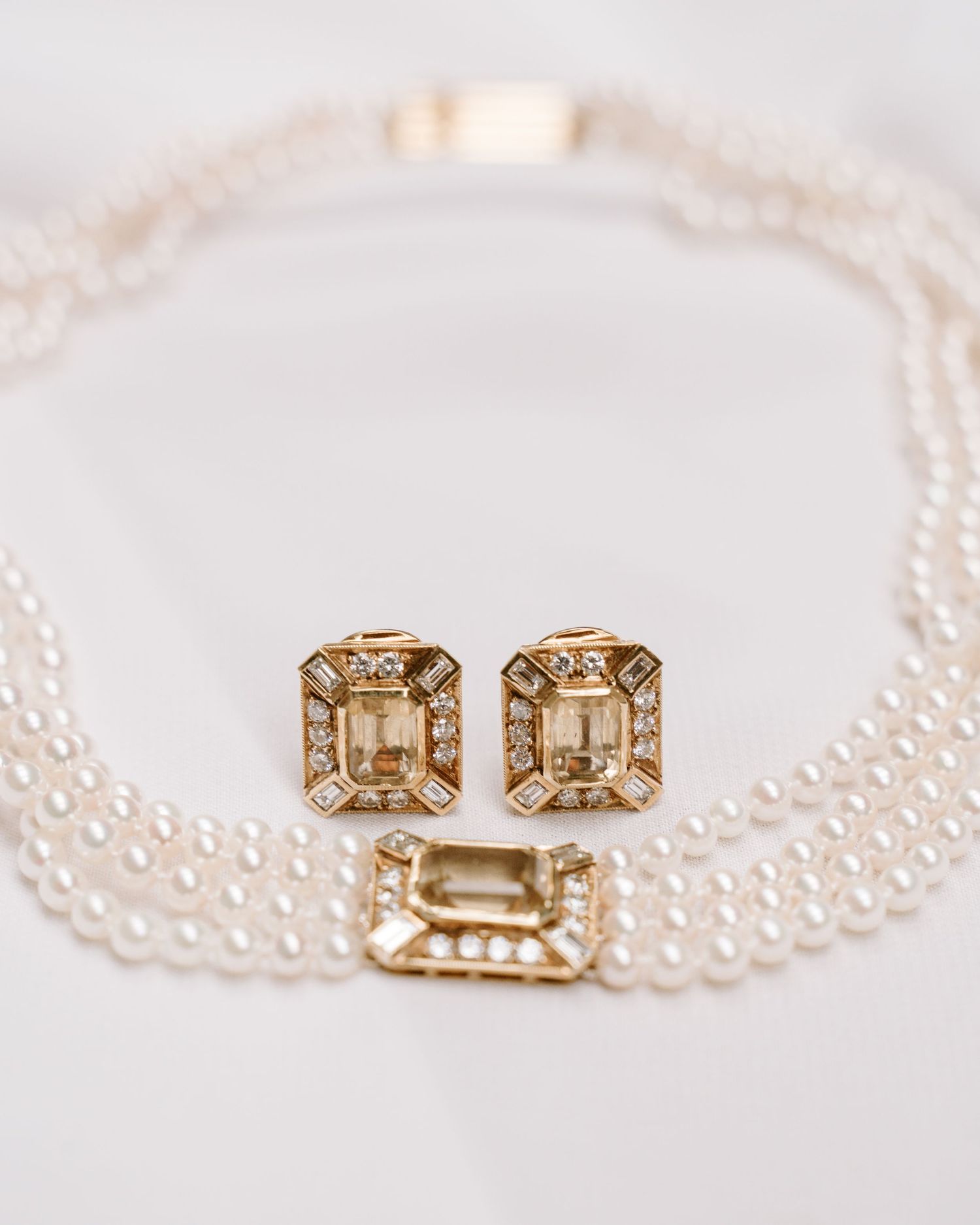 Elegant pearl choker necklace with gold diamond-framed clasp displayed alongside matching champagne crystal stud earrings.