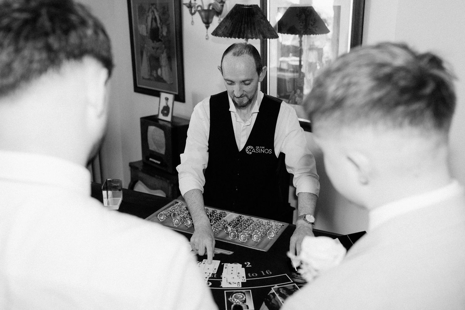 Black and white photo of a dealer managing a casino card game table at an indoor event.