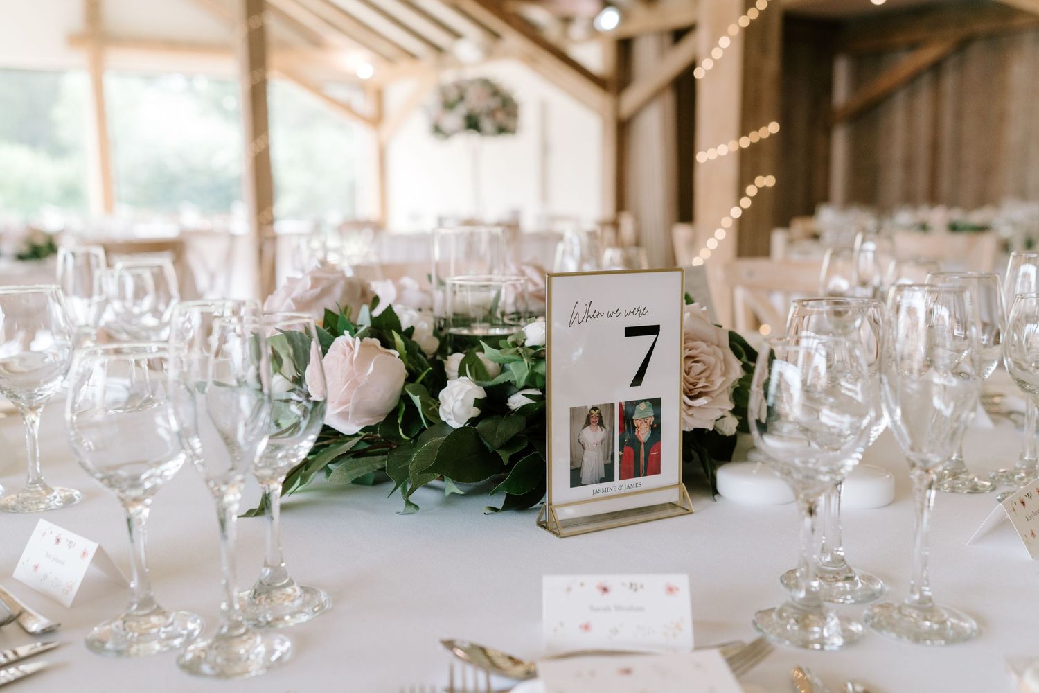 Elegant wedding reception table with floral centerpiece, wine glasses, and table number 7 sign in a rustic barn venue.