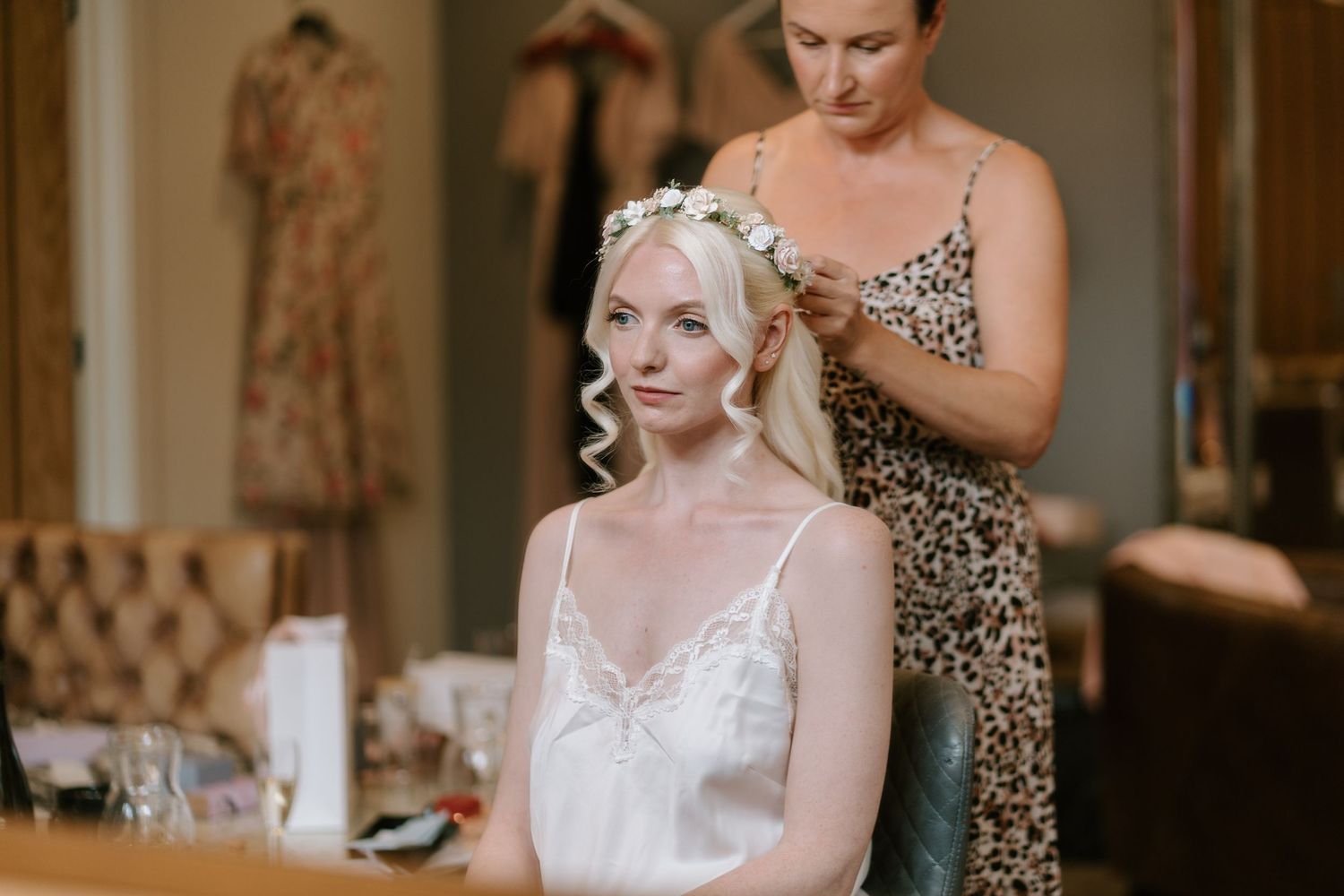 Bride getting flower crown placed in wavy blonde hair by stylist in leopard print dress before wedding.