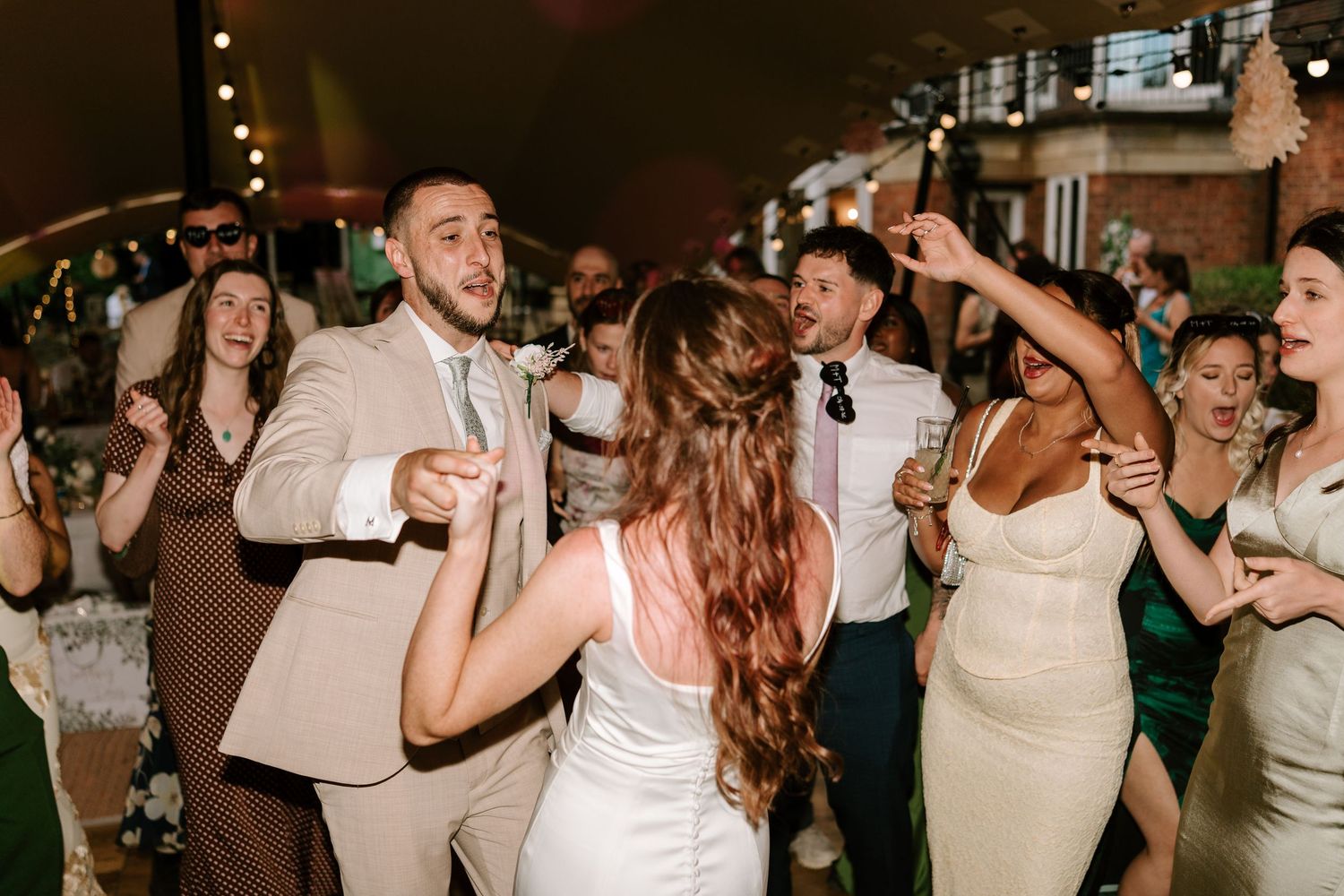 Bride and groom dancing joyfully with wedding guests at a lively outdoor evening reception.