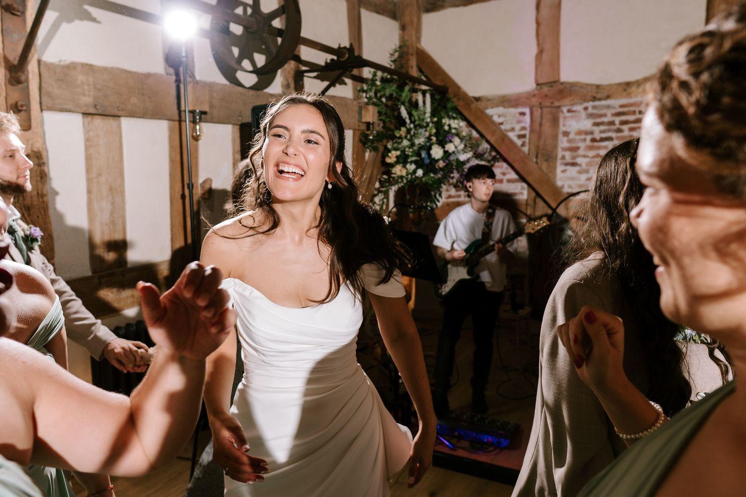 Bride dancing joyfully with guests at a rustic barn wedding reception, wearing a white gown.