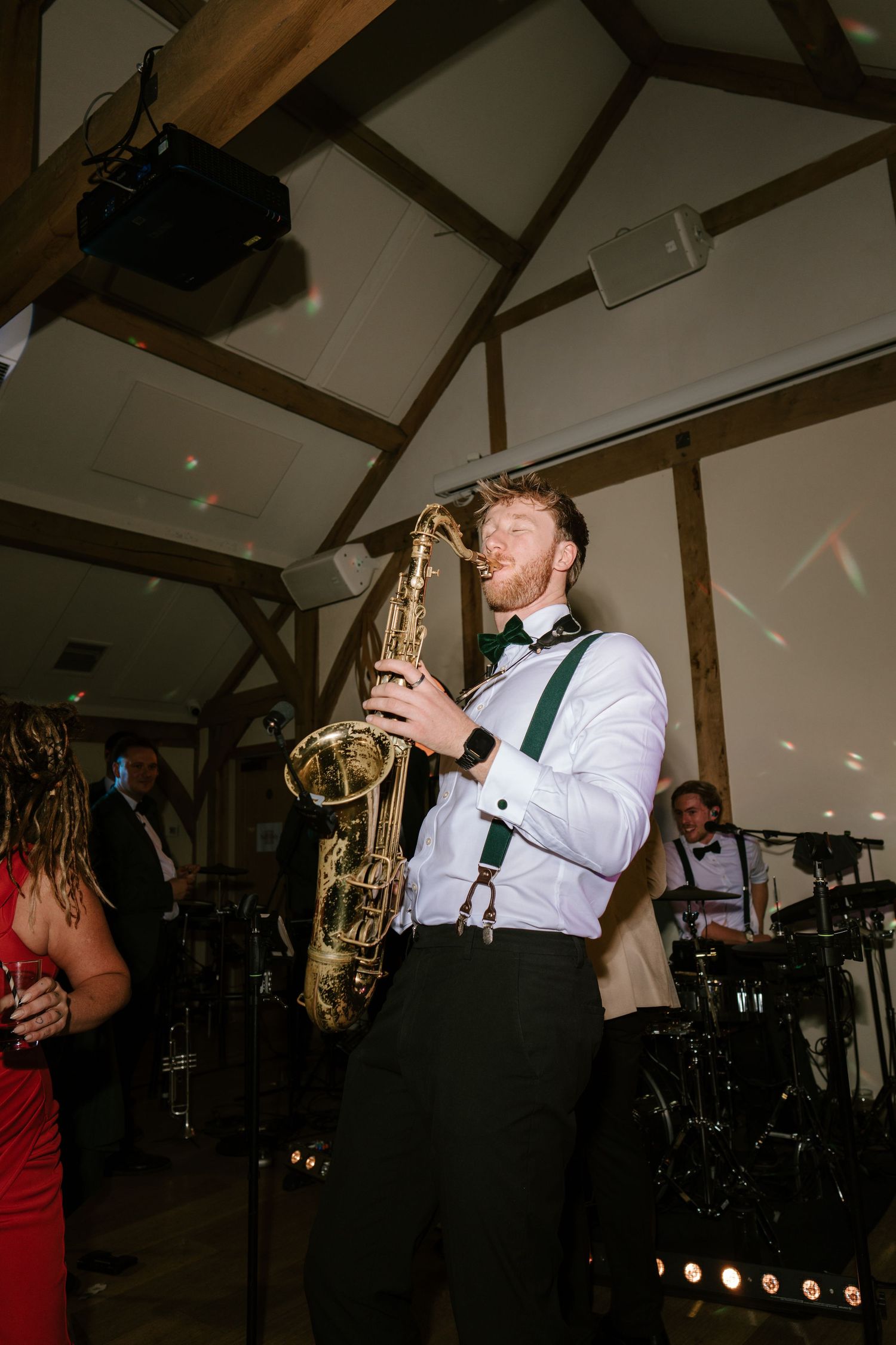 A saxophonist in white shirt and green suspenders performs at an elegant wedding reception venue.