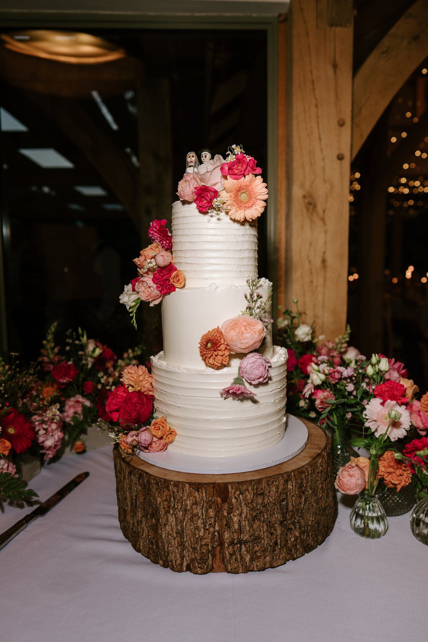 Three-tier white wedding cake with bright fresh flowers in the Knot Barn at Brinsop Court