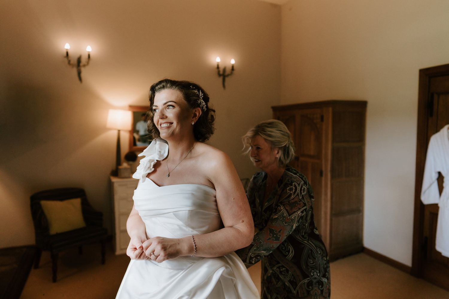 Bride smiling as she is fastened into her wedding dress at Brinsop Court