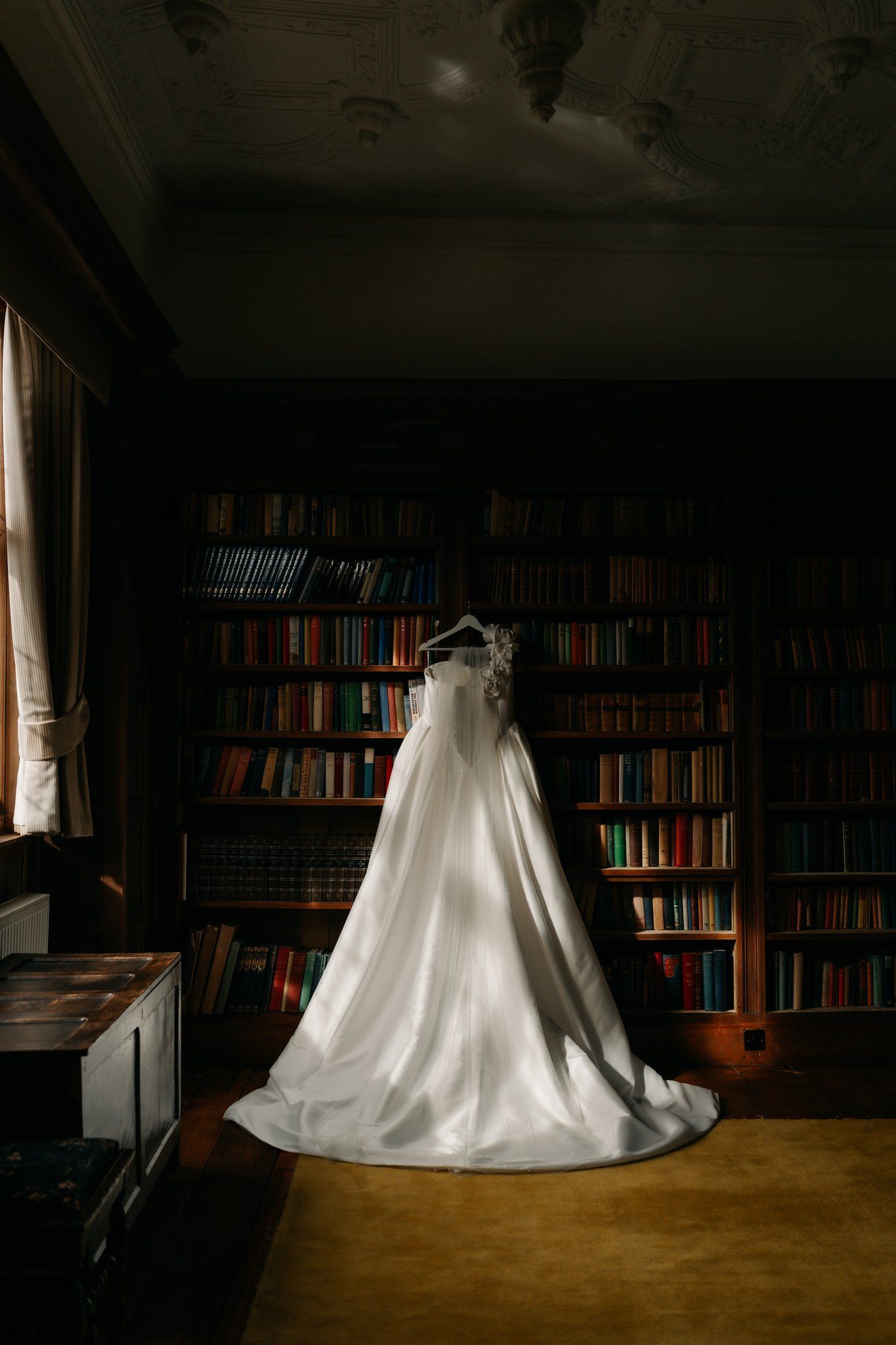 Satin TDR bridal wedding dress hanging in the oak-panelled library at Brinsop Court wedding venue