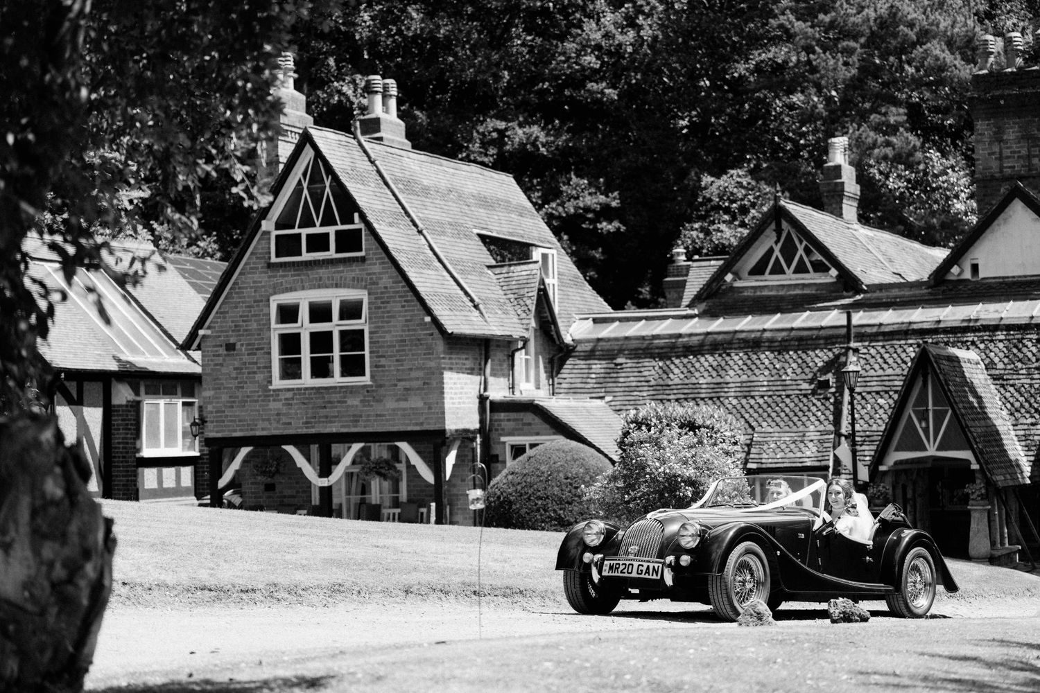 Black and white photo of classic vintage car parked outside rustic Tudor-style wedding venue.