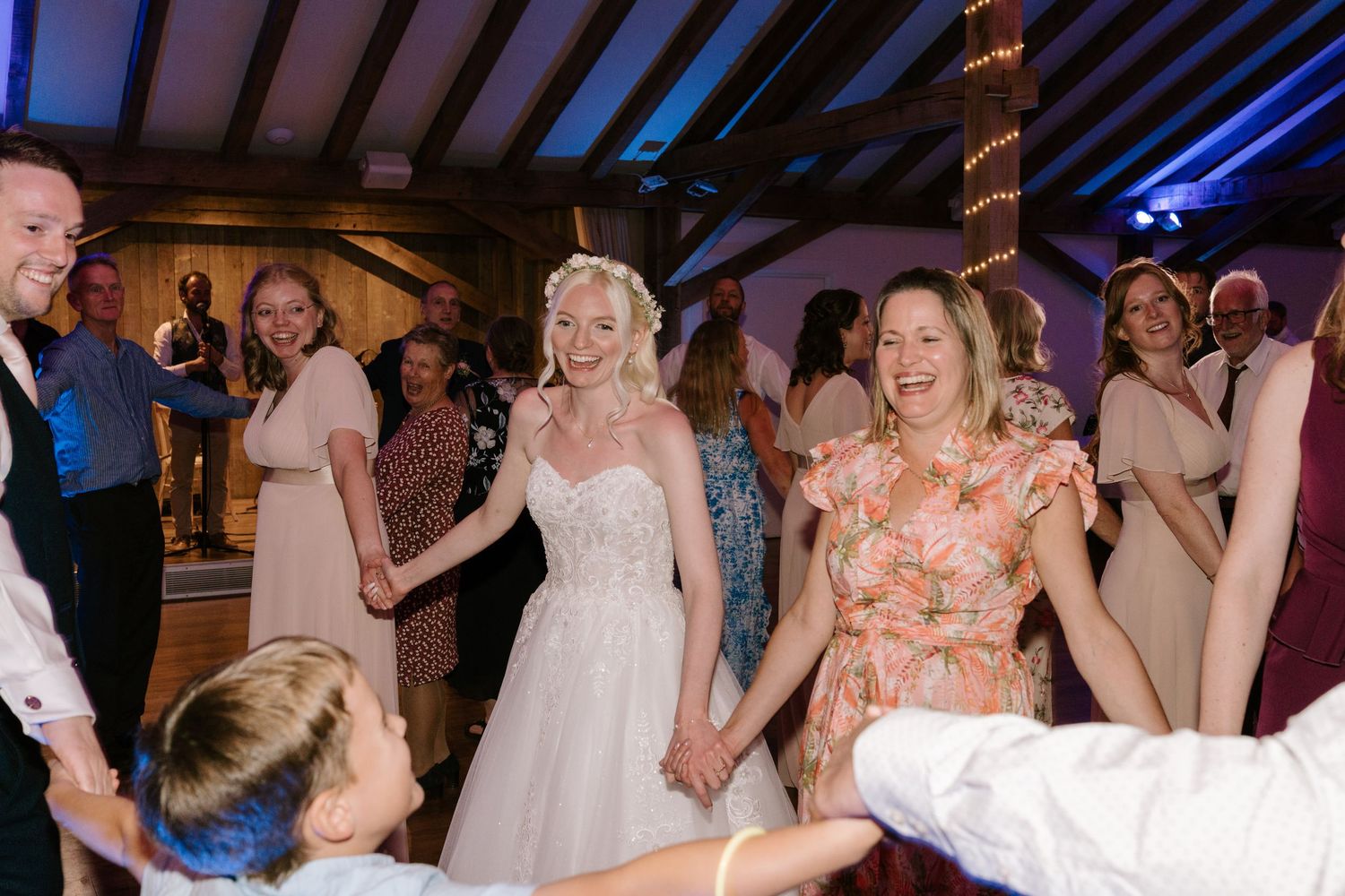 Bride in white gown holds hands with guests dancing joyfully at a wedding reception celebration.