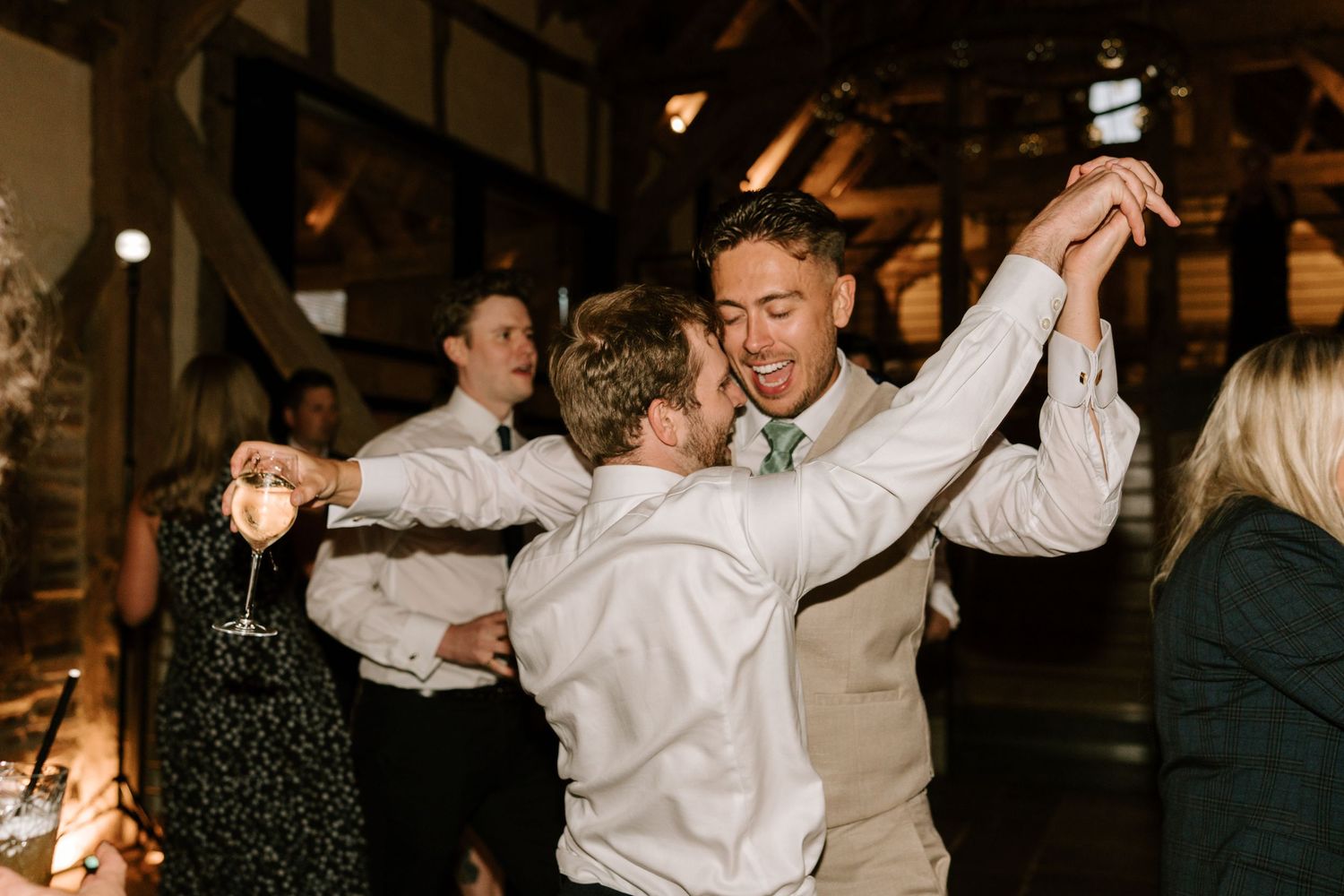 Energetic wedding reception dance floor moment with groom celebrating with guests in barn venue.