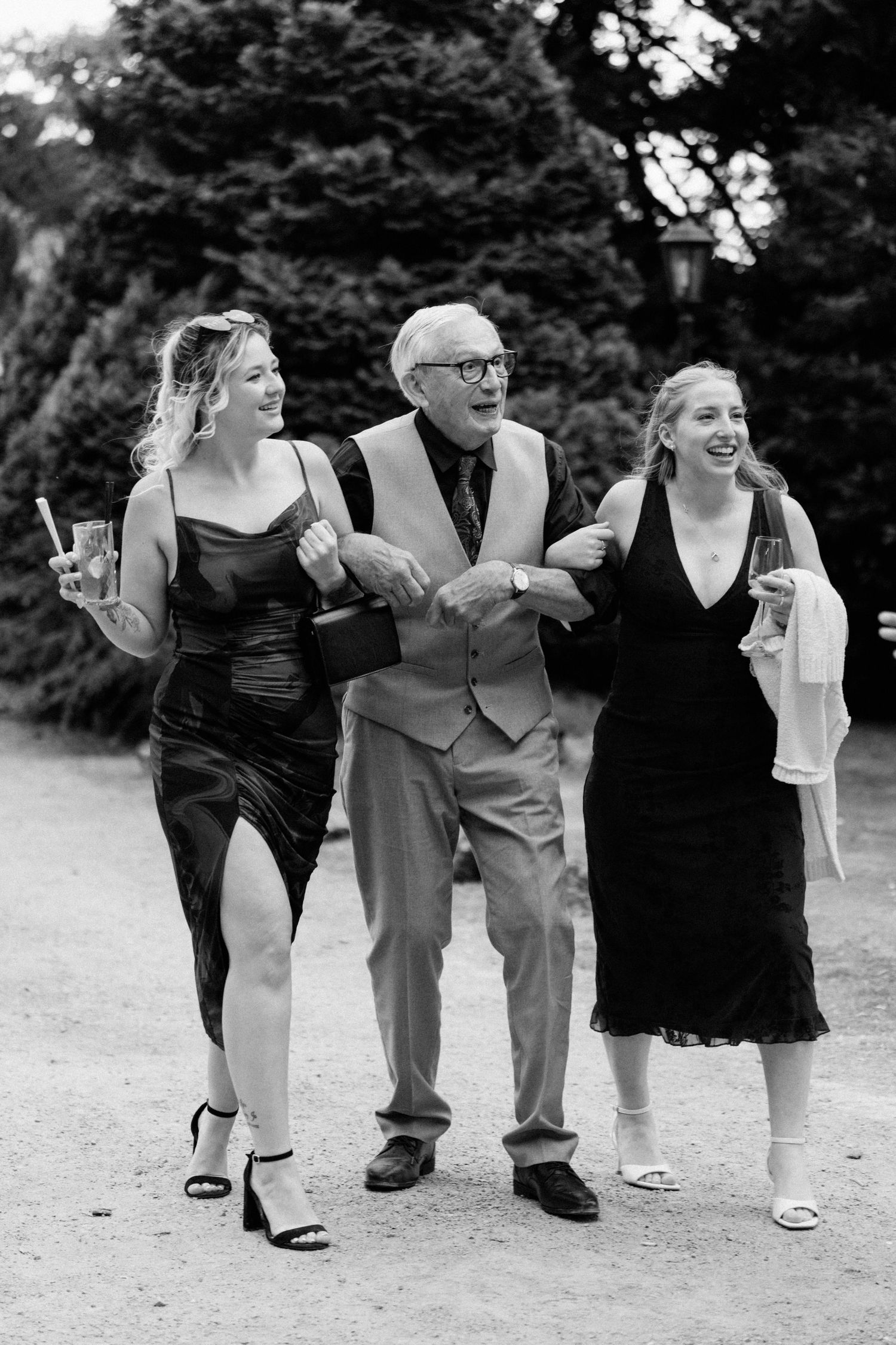Black and white photo of an older man escorted by two young women at a wedding.