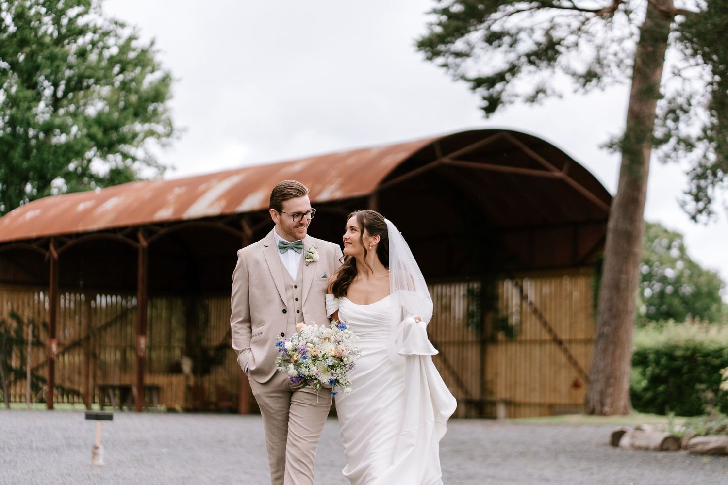 Bride and groom walking together outside rustic barn venue on their wedding day.