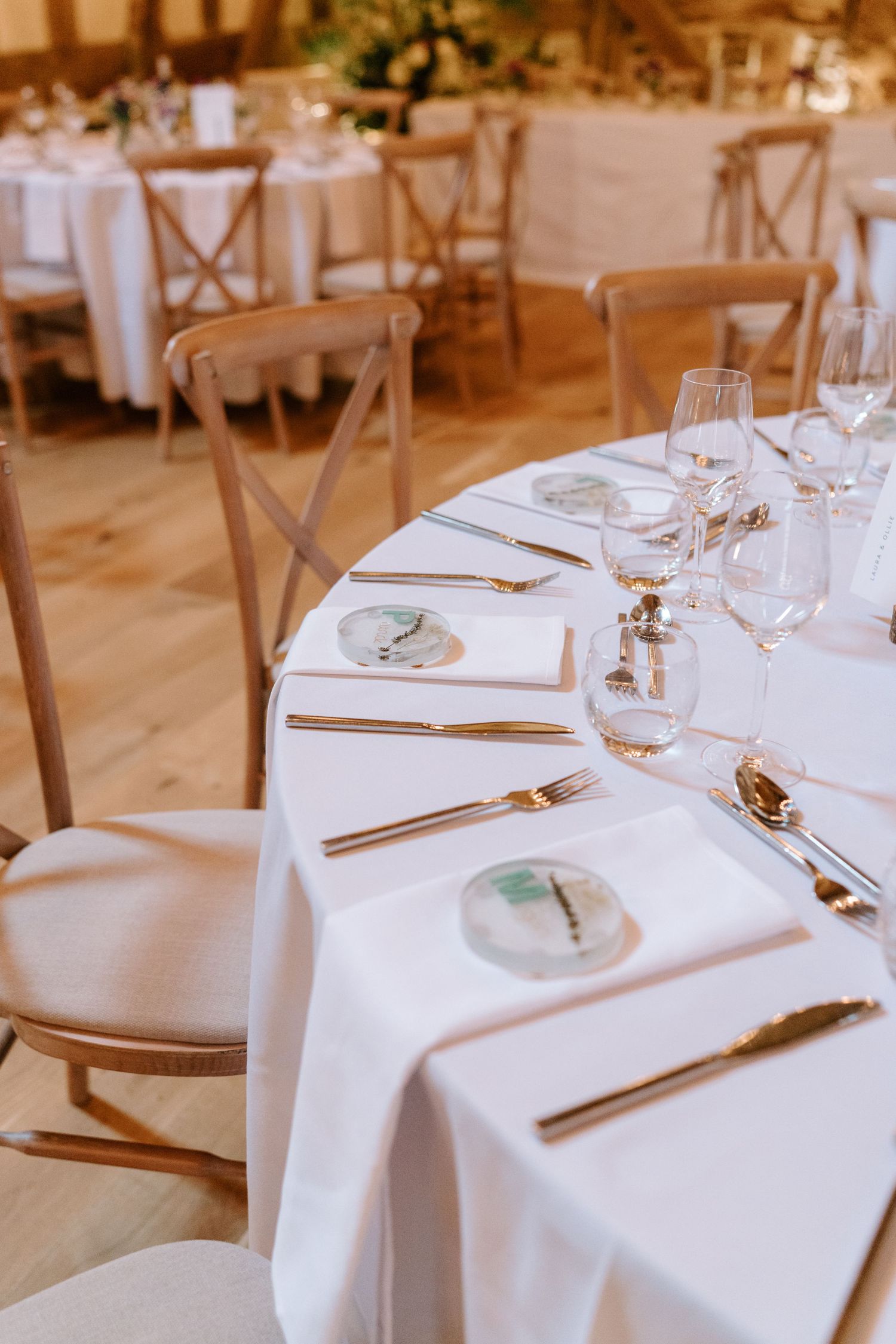 Elegant wedding reception table set with gold cutlery, crystal glasses, and decorative plates on white linen in a rustic barn venue.