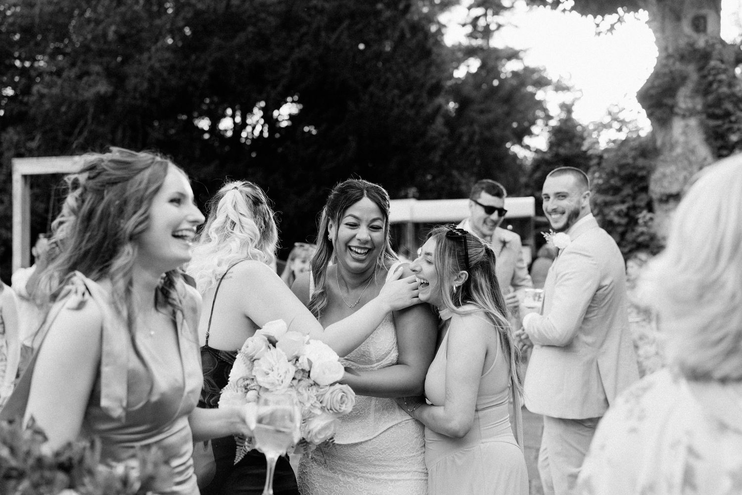 Bridesmaids laughing and embracing joyfully at an outdoor wedding reception in black and white.