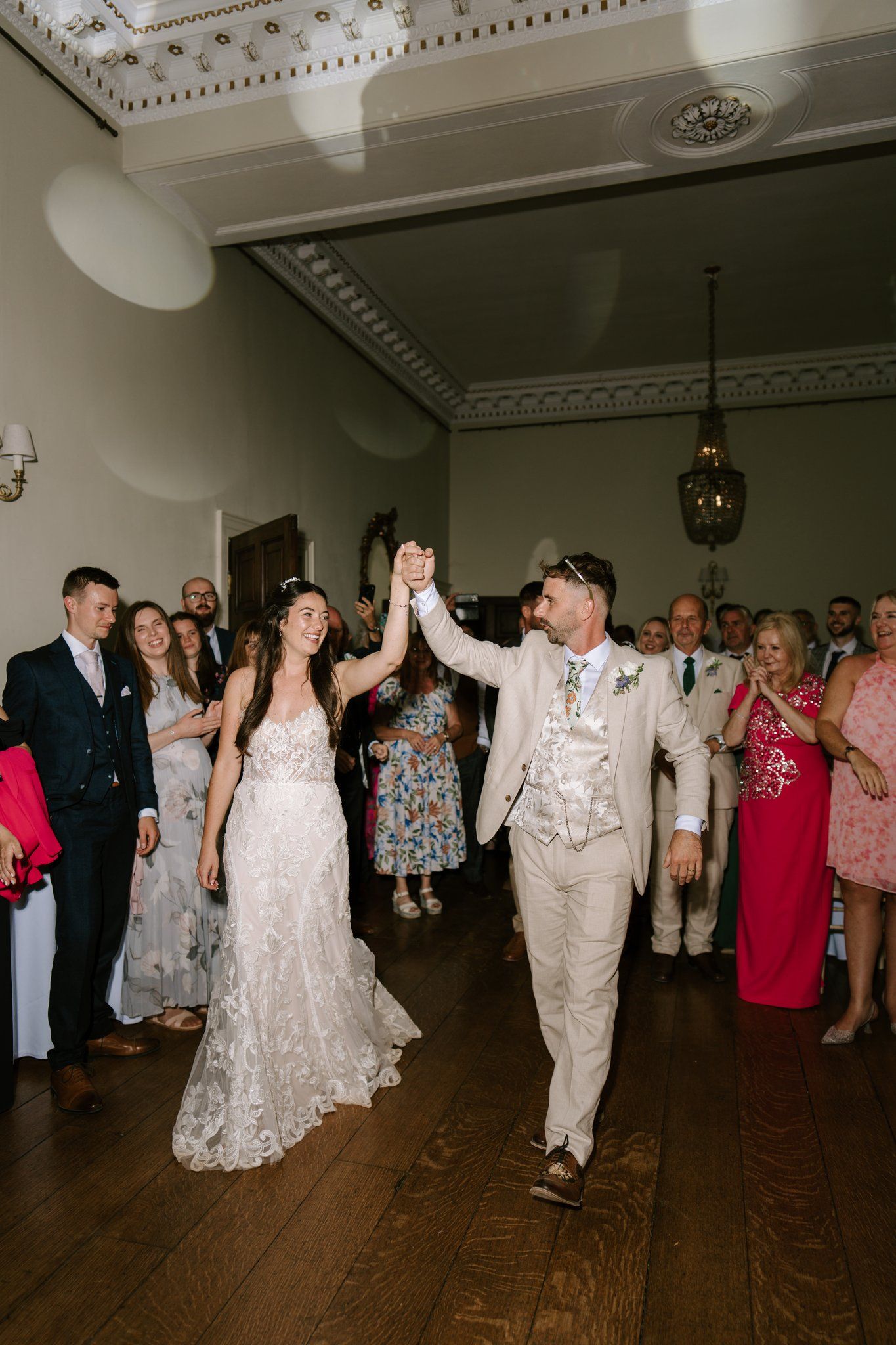 Bride and groom raise hands together on dance floor surrounded by wedding guests in elegant venue.