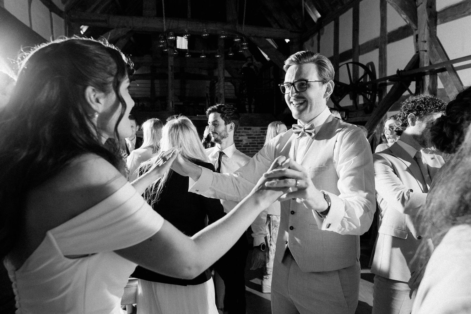 Black and white photo of couple dancing joyfully at a wedding reception in a rustic barn venue.