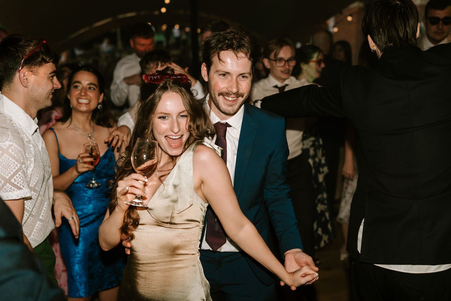 Joyful wedding guests dancing and celebrating together at lively indoor wedding reception party.