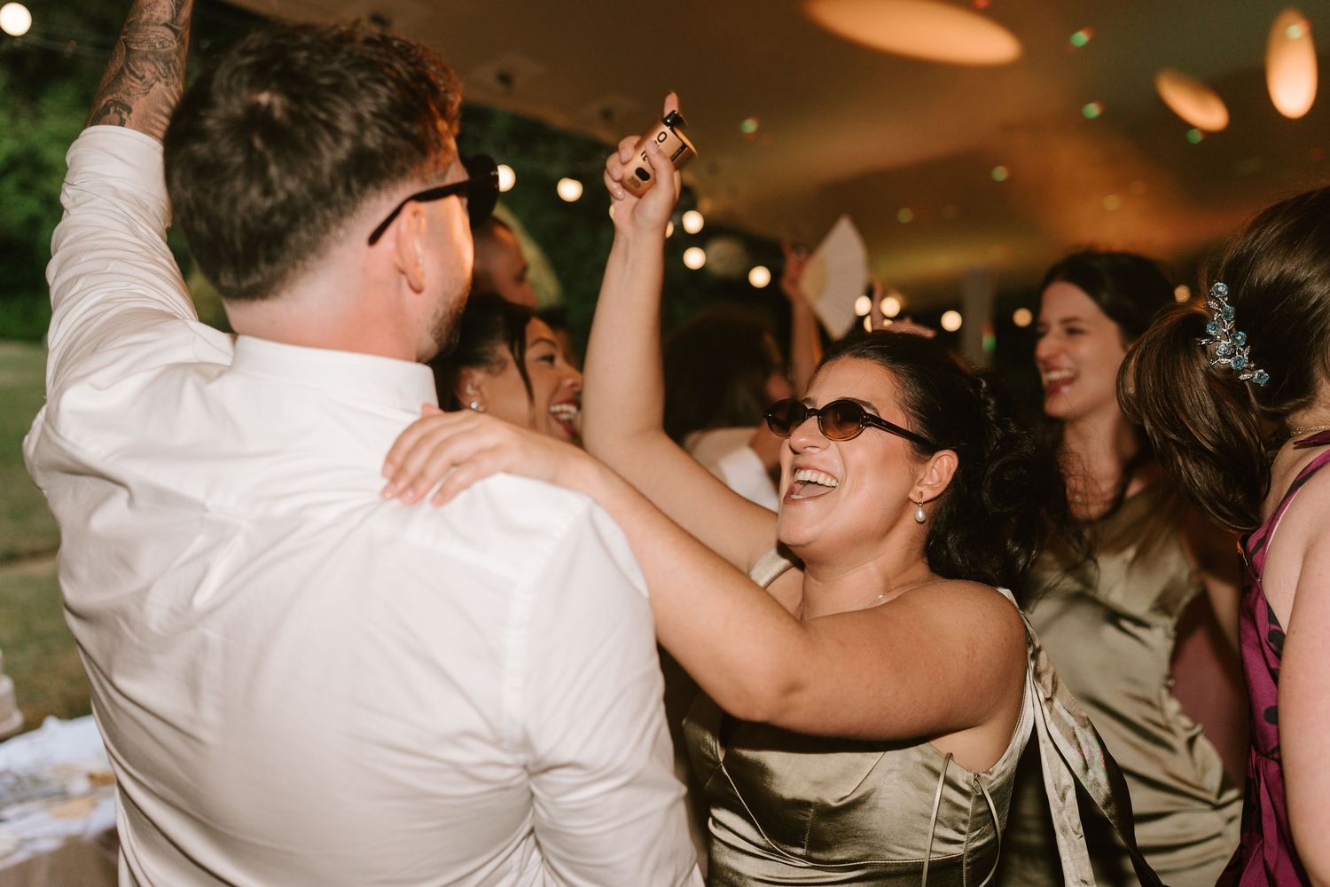 Wedding guests dancing joyfully together at lively outdoor reception celebration.
