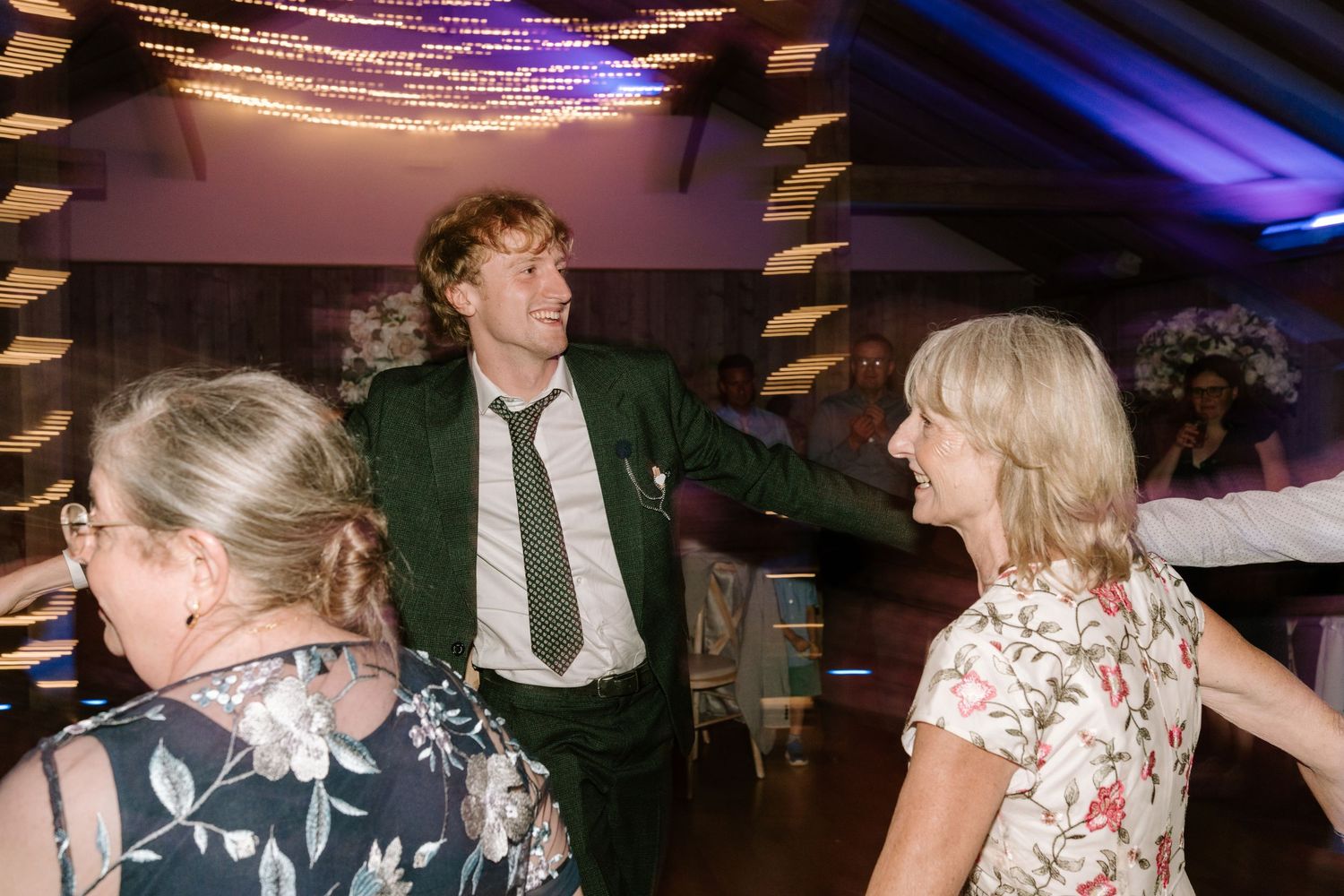 Man in green suit dancing with women at a wedding reception party in a decorated venue.