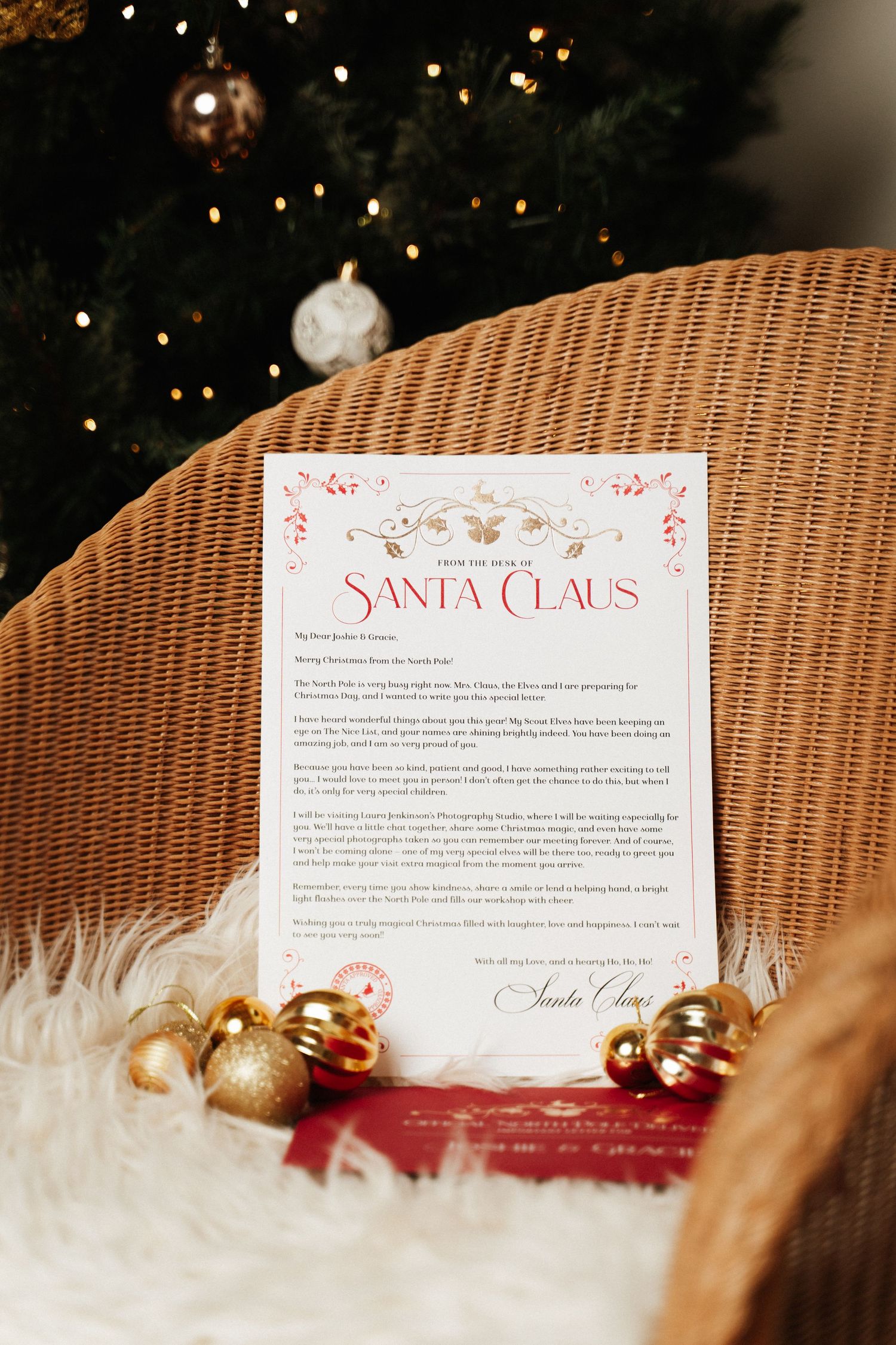 A personalized letter from Santa Claus displayed on a wicker chair with gold Christmas ornaments and a tree in the background.