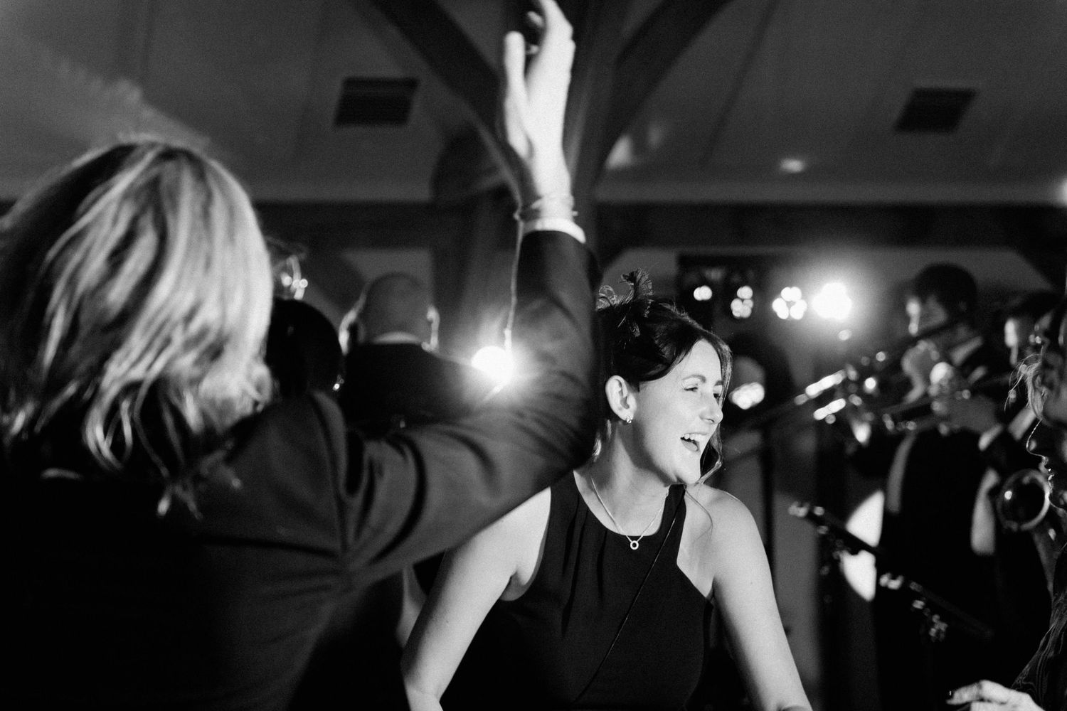 Black and white photo of a woman smiling and dancing at a formal event with bright lights in the background.