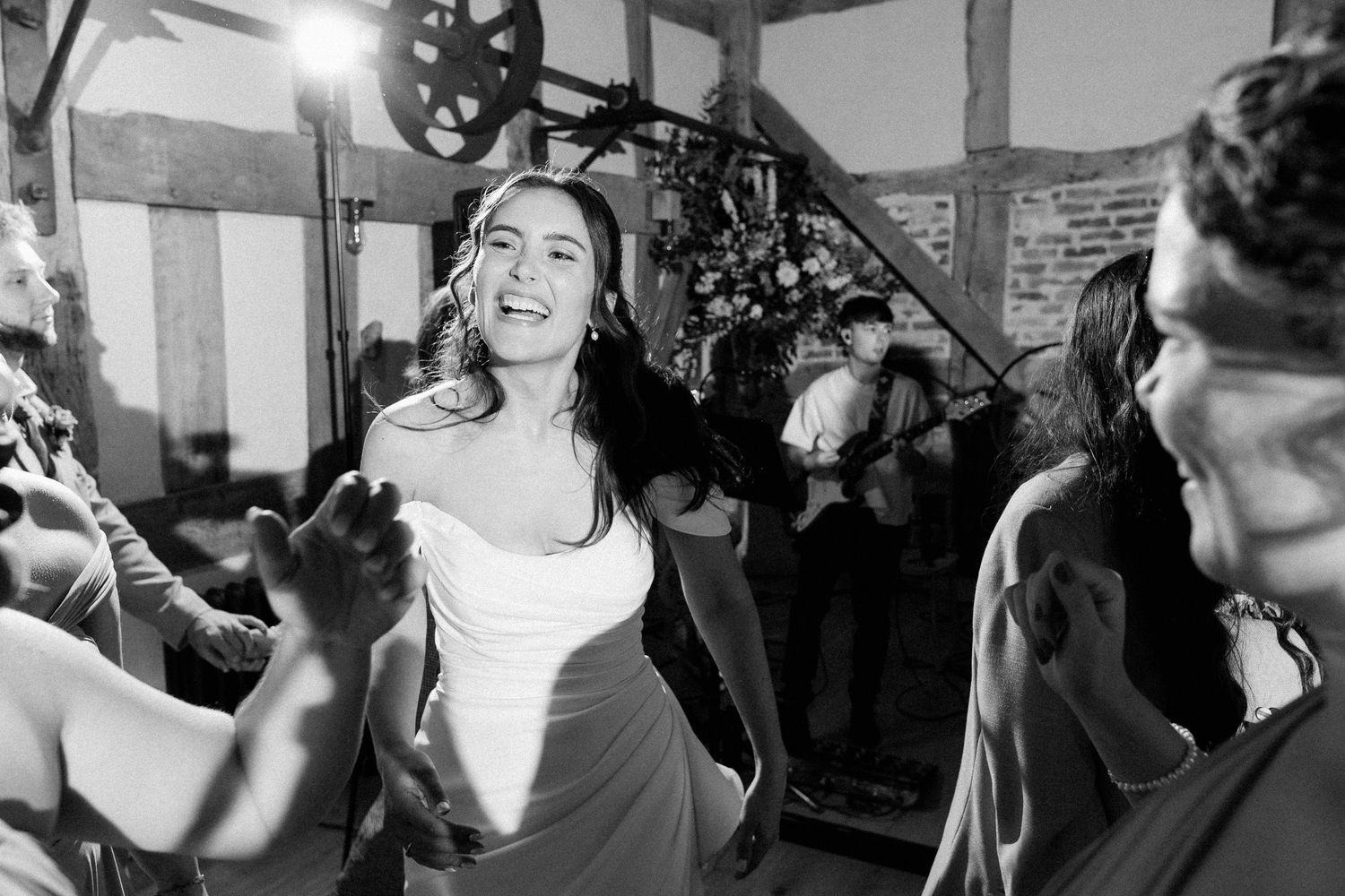 Black and white photo of a joyful bride dancing energetically at her wedding reception with guests celebrating around her.