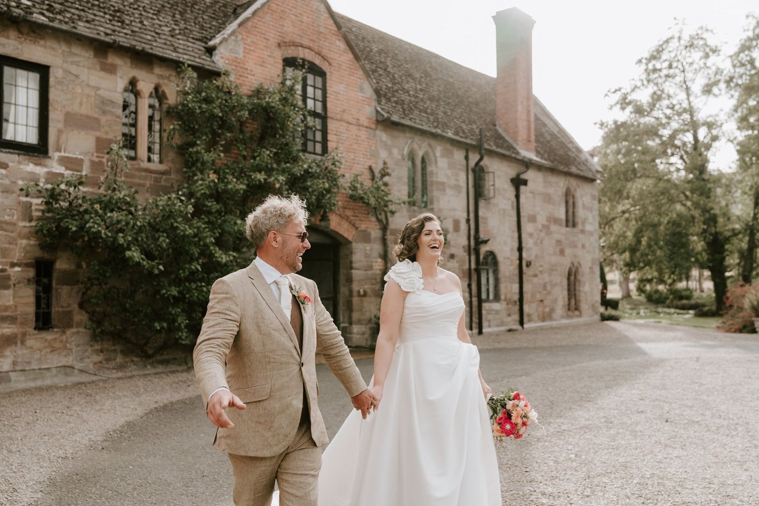 Bride and groom walking hand in hand beside the sandstone walls of Brinsop Court
