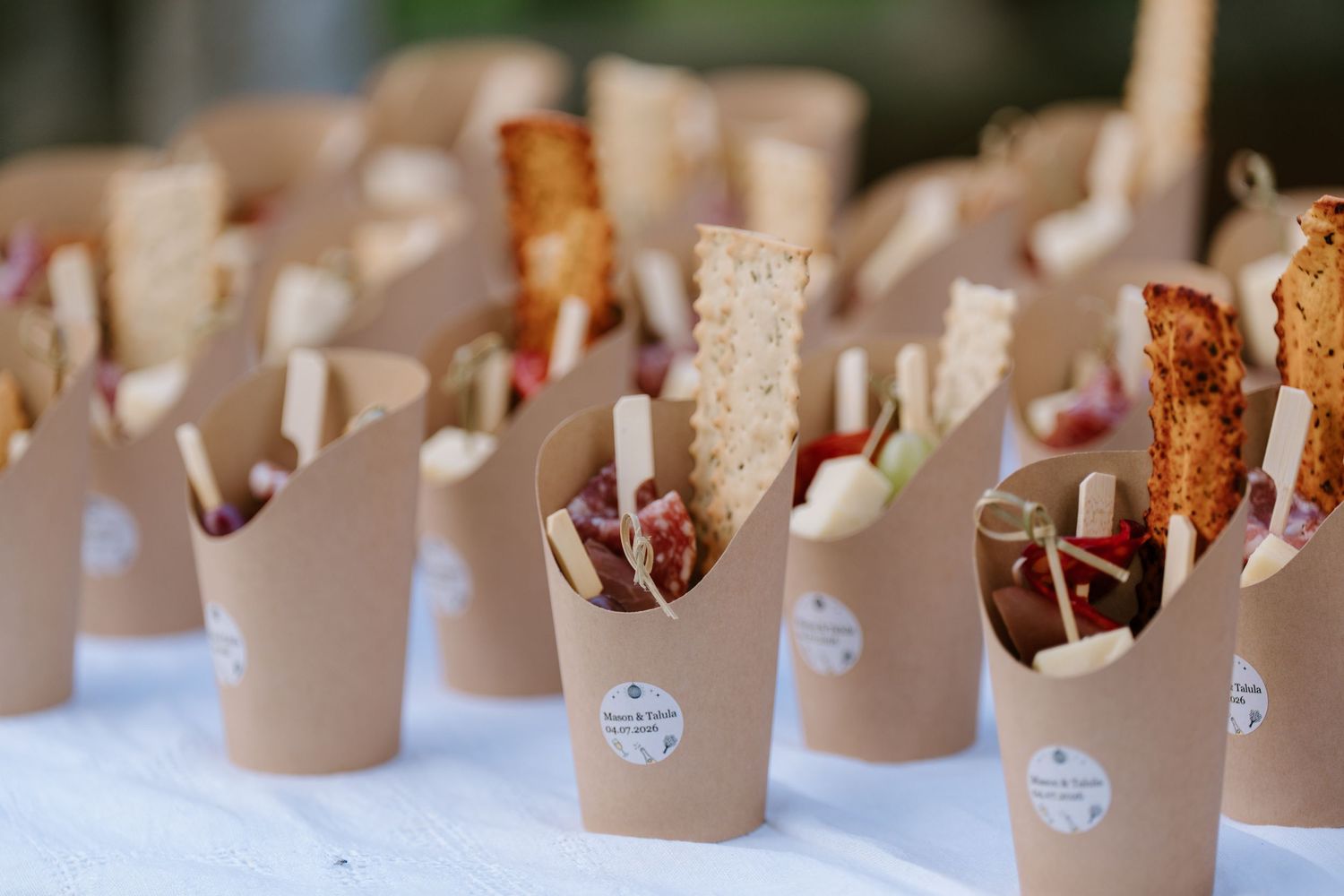 Rows of kraft paper cones filled with appetizers and charcuterie at wedding catering.