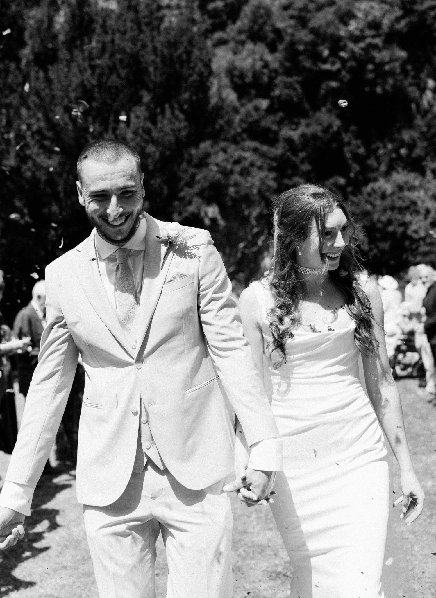 Black and white photo of smiling bride and groom walking hand in hand after outdoor wedding ceremony.