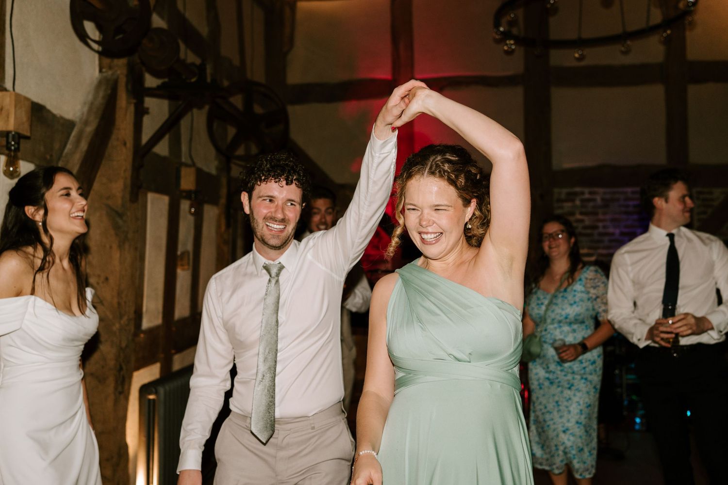 Wedding guest in sage green dress being spun by a partner on the dance floor during a lively barn wedding reception.
