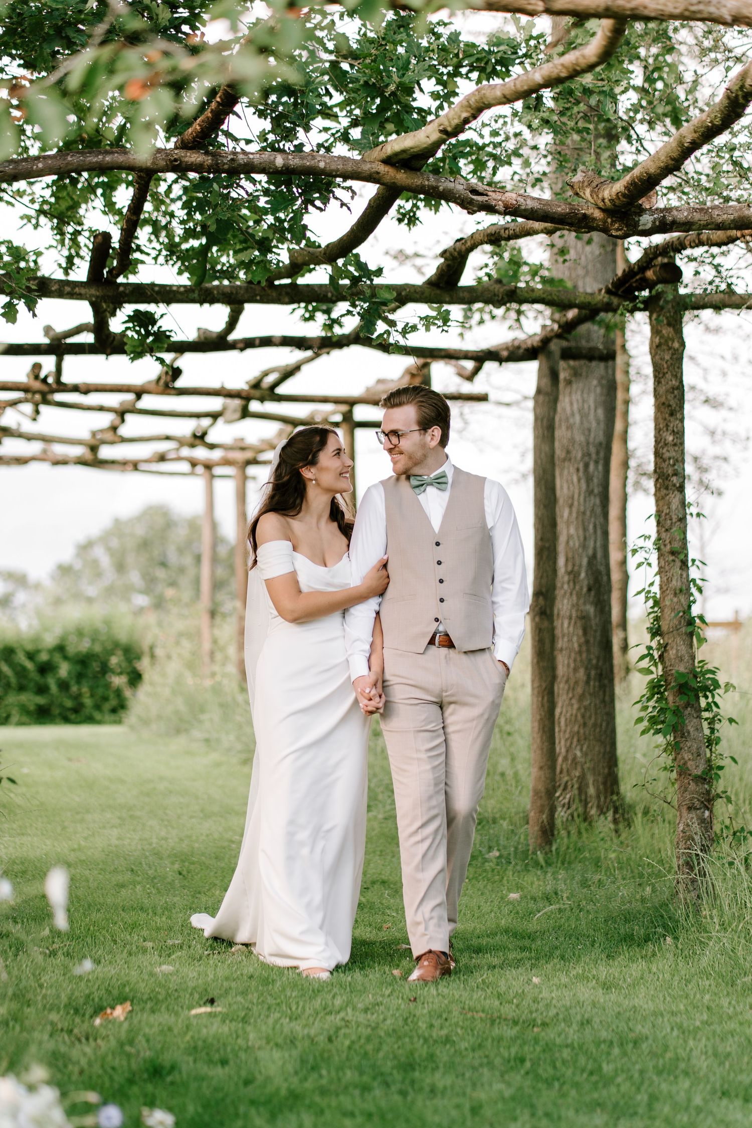 Bride and groom sharing a romantic moment under a wooden pergola surrounded by lush garden greenery.