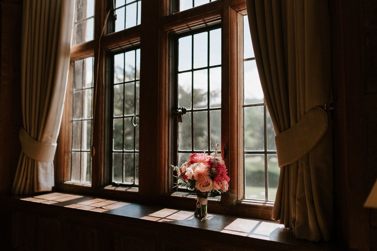 bouquet on windowsill: Pink, coral and orange dahlia wedding bouquet on an oak windowsill at Brinsop Court