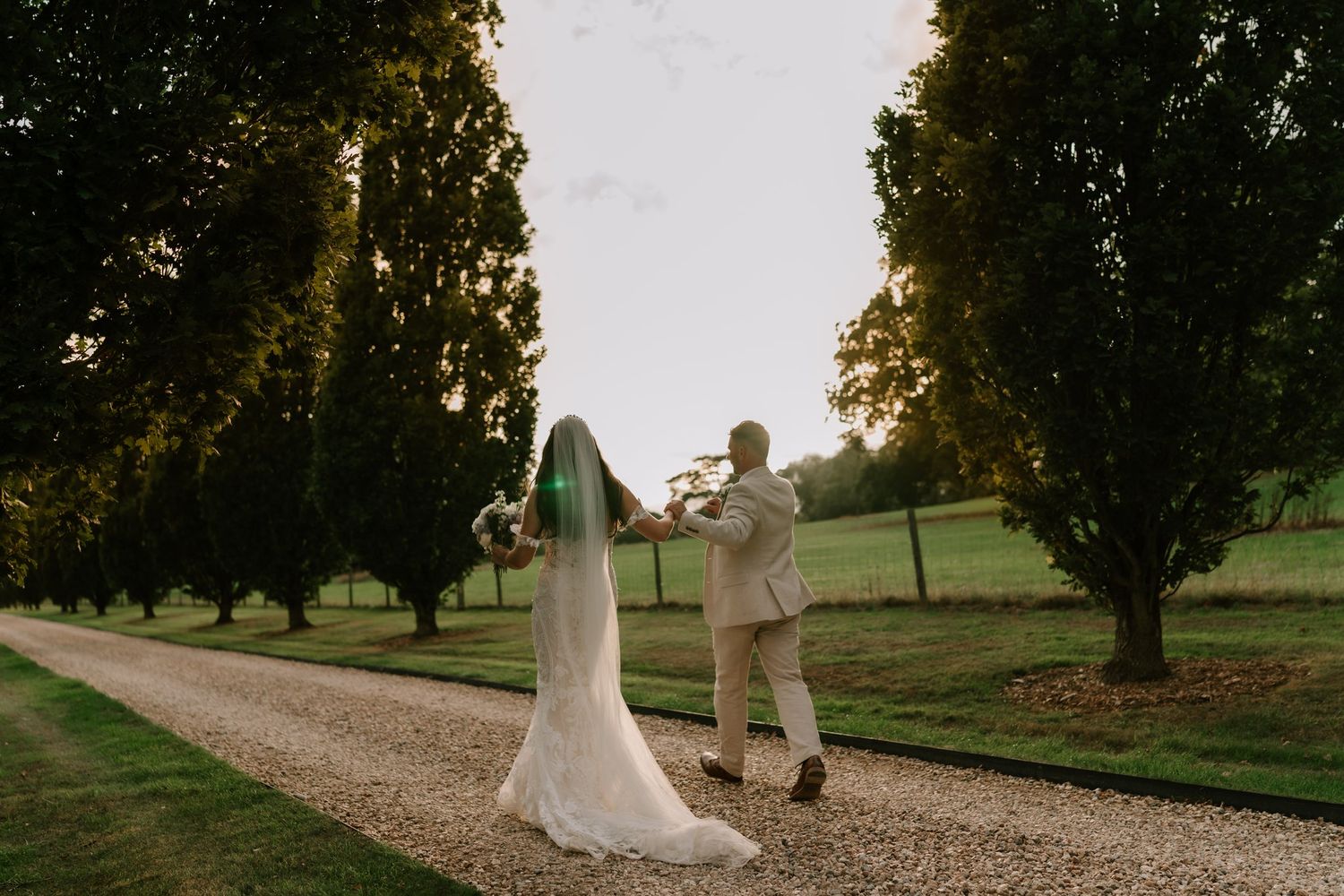 Bride and groom dancing on a tree-lined gravel path at golden hour during an outdoor wedding celebration.