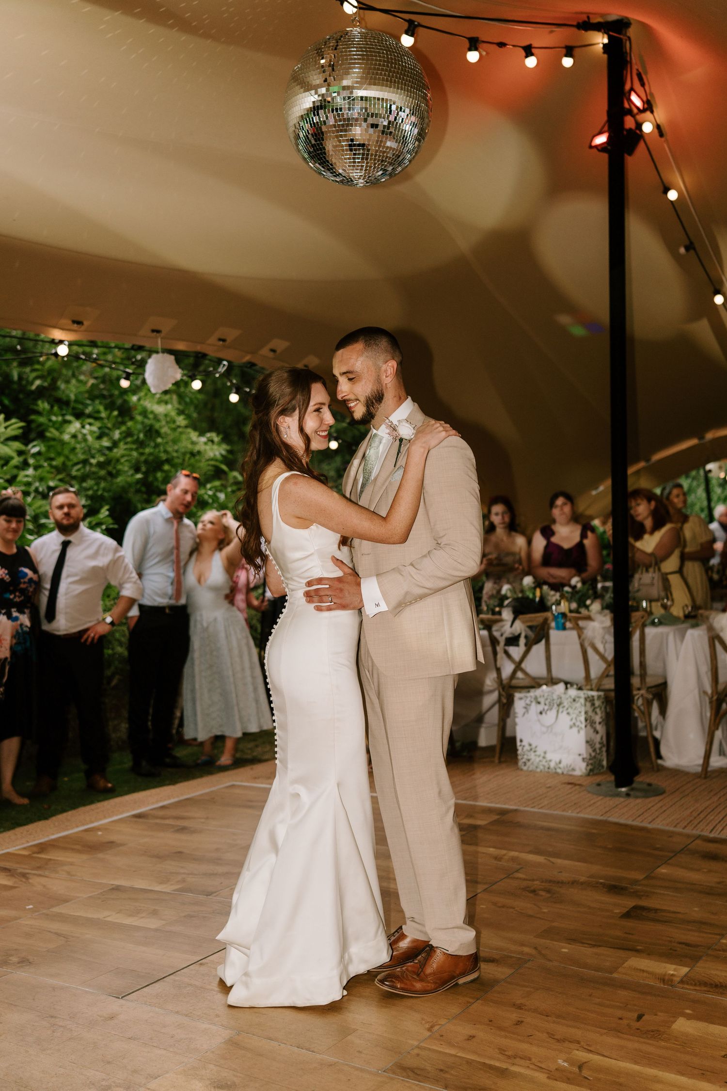Bride and groom share their first dance under a disco ball at an outdoor wedding reception.
