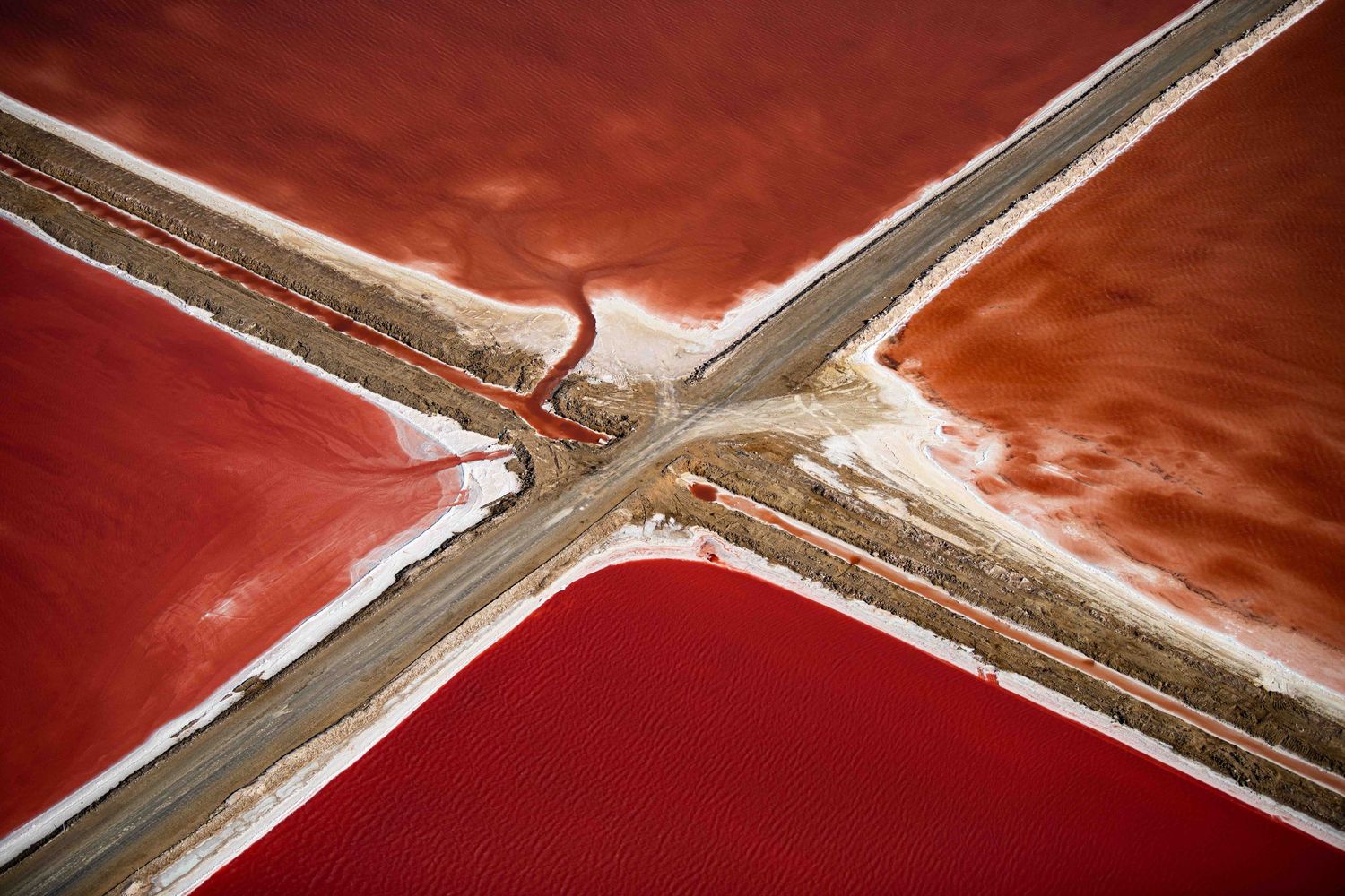 Aerial view of vibrant red salt evaporation ponds divided by intersecting roads in Namibia.