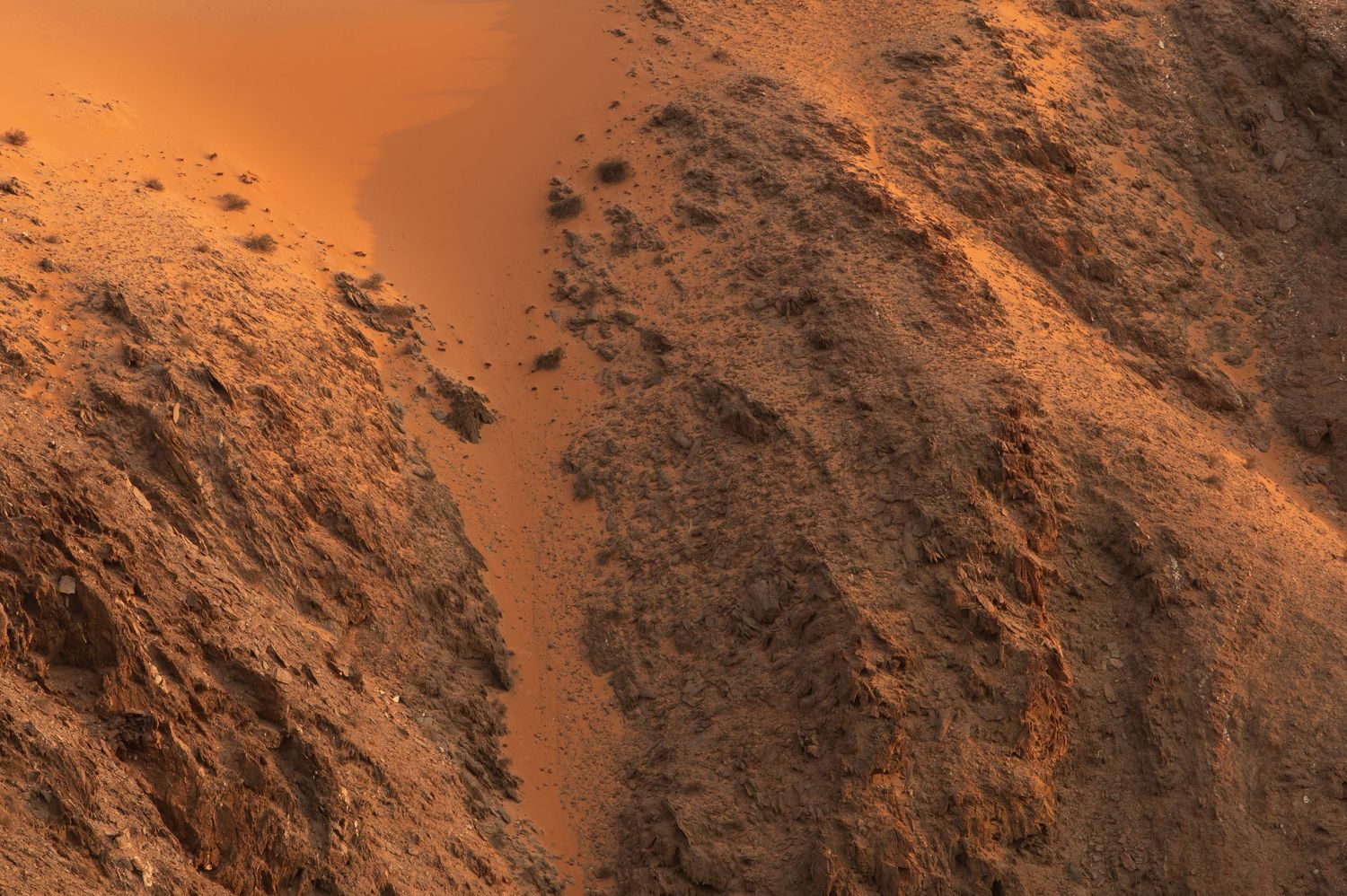 Aerial view of dramatic orange sand dunes and rocky terrain in Namibian desert landscape.