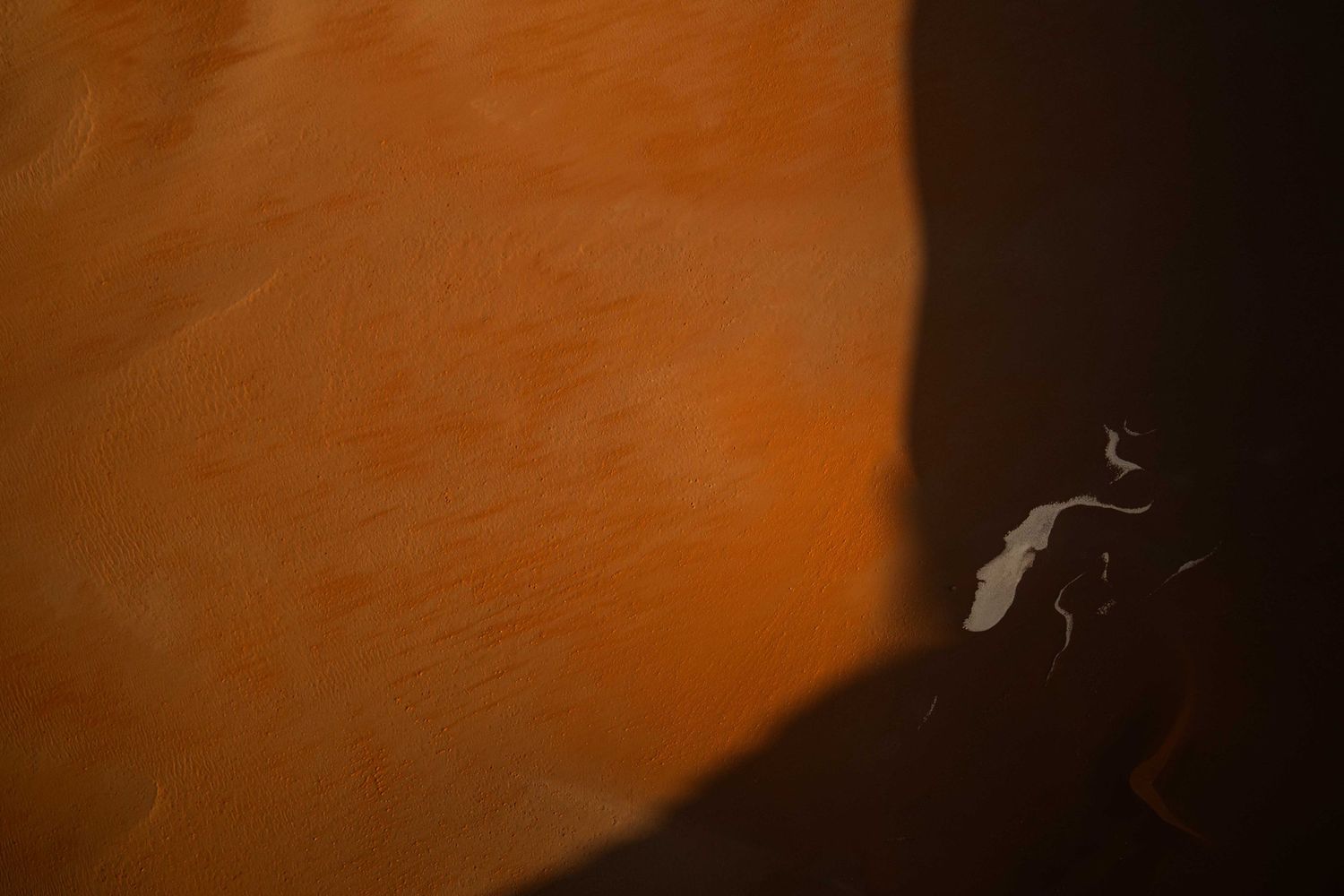 A lone figure casts a shadow on a vast orange sand dune in the Namib Desert.