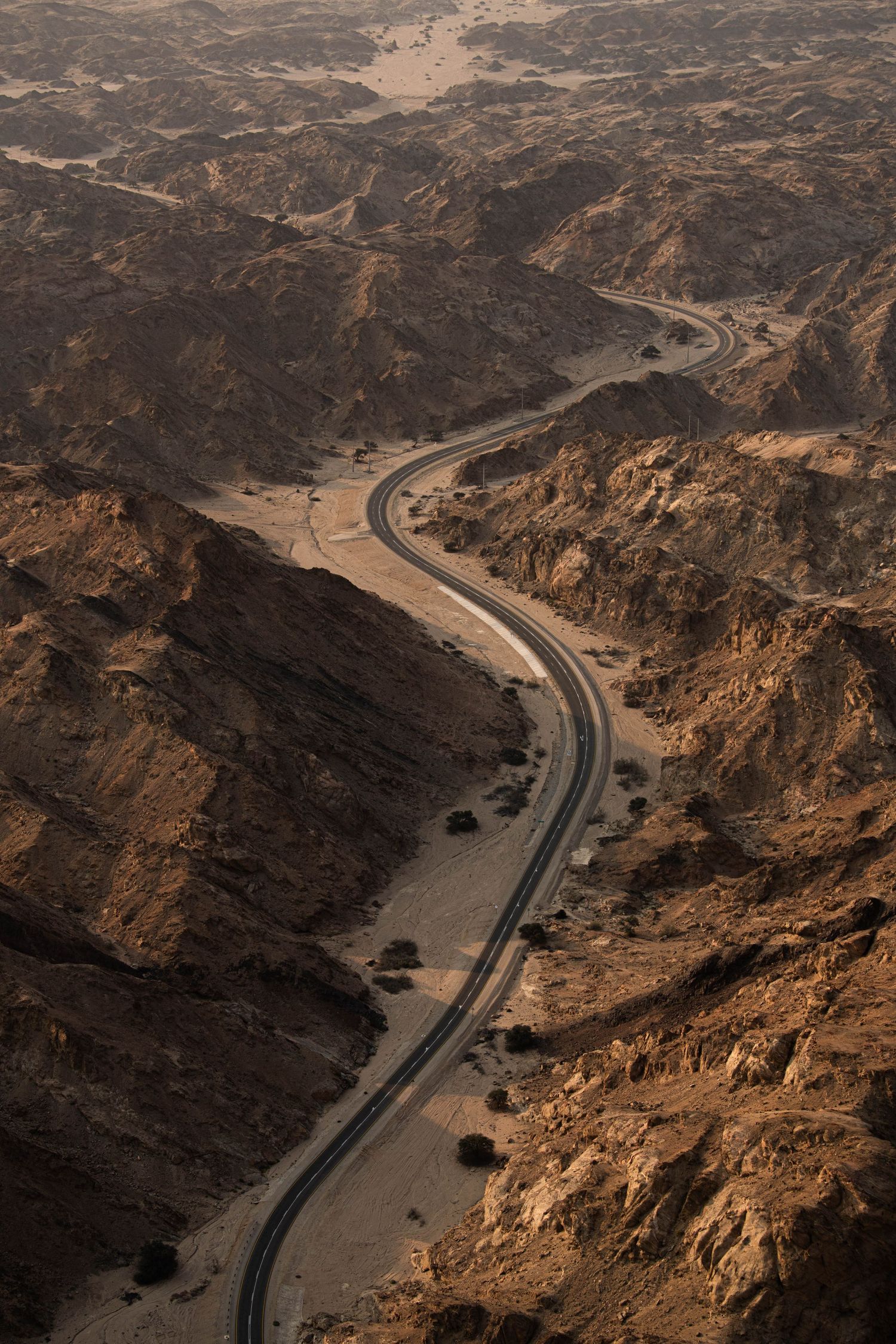 Aerial view of winding road cutting through dramatic rocky desert canyon landscape at dusk.