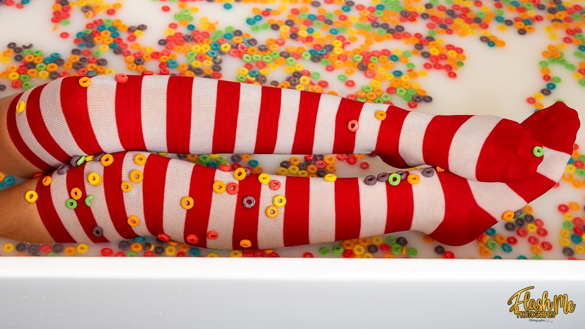 Legs wearing red and white striped knee-high socks submerged in a bath filled with colorful cereal.