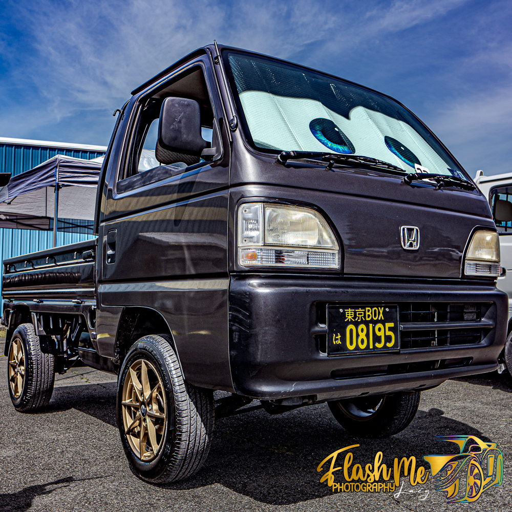 Black Honda Acty mini kei truck with gold wheels and Tokyo license plate at an auto show.