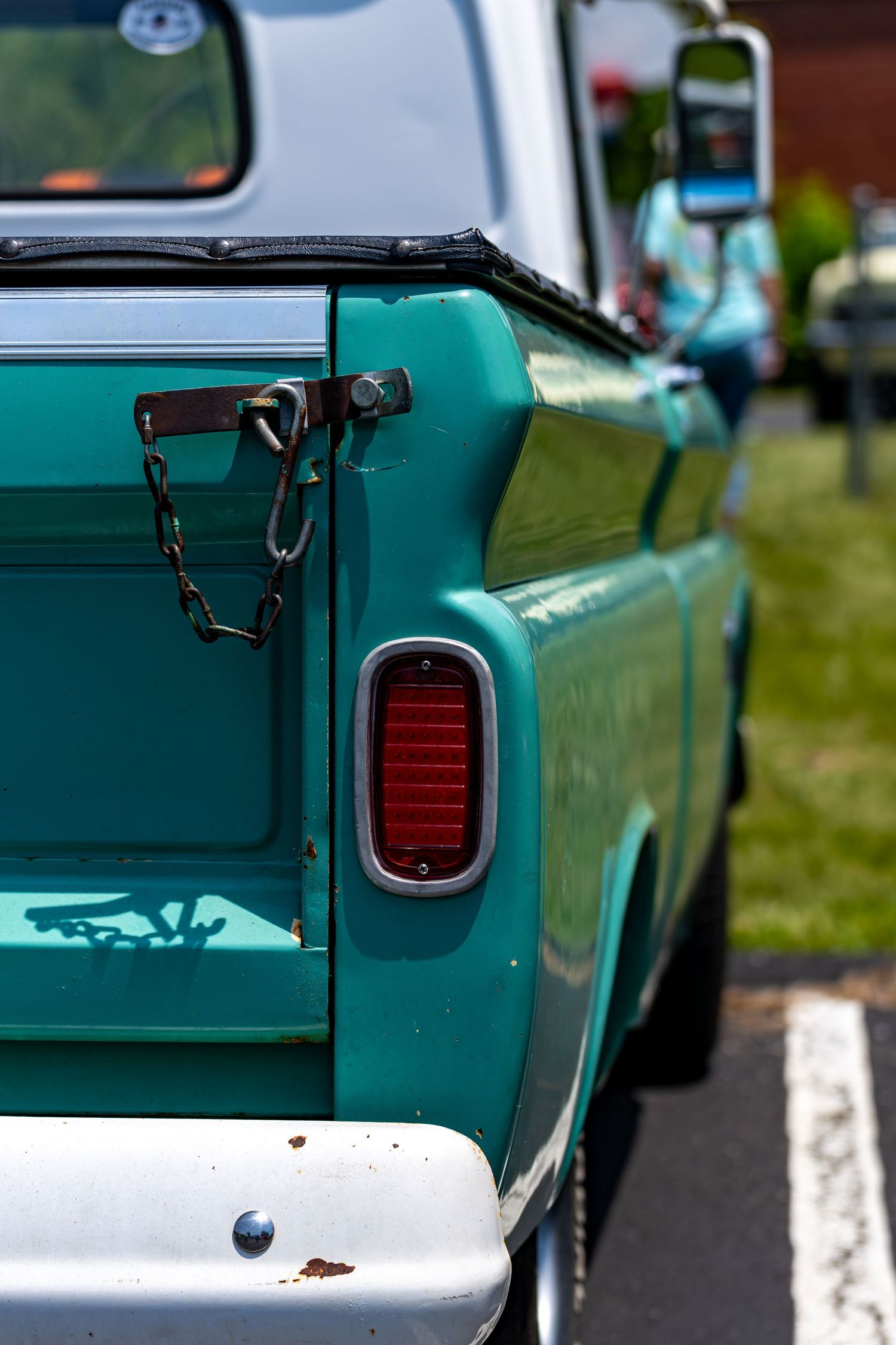 Vintage teal pickup truck rear corner with chrome tail light and chain tailgate latch.