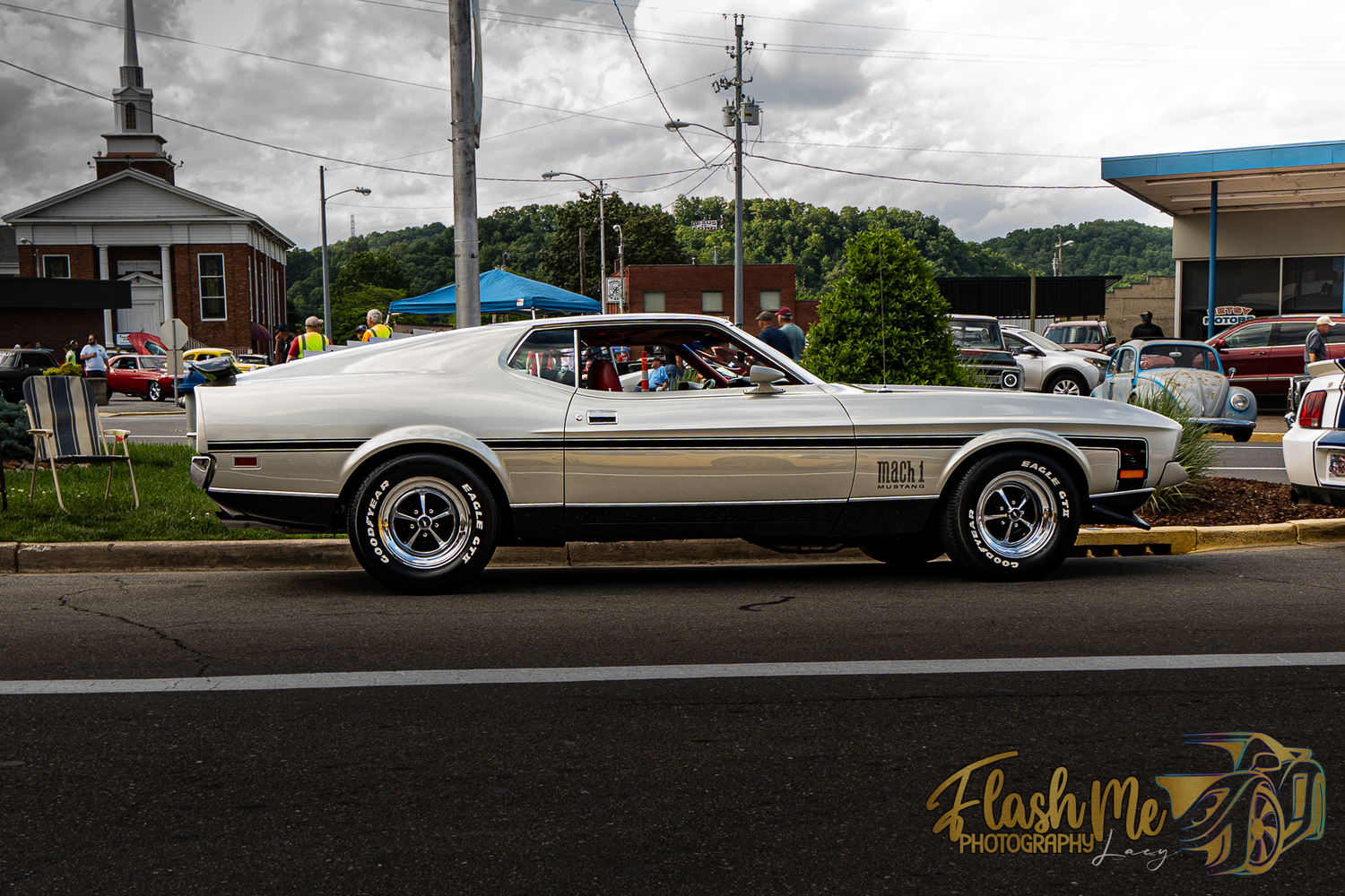 Classic white Ford Mustang Mach 1 driving on a street at a car show.